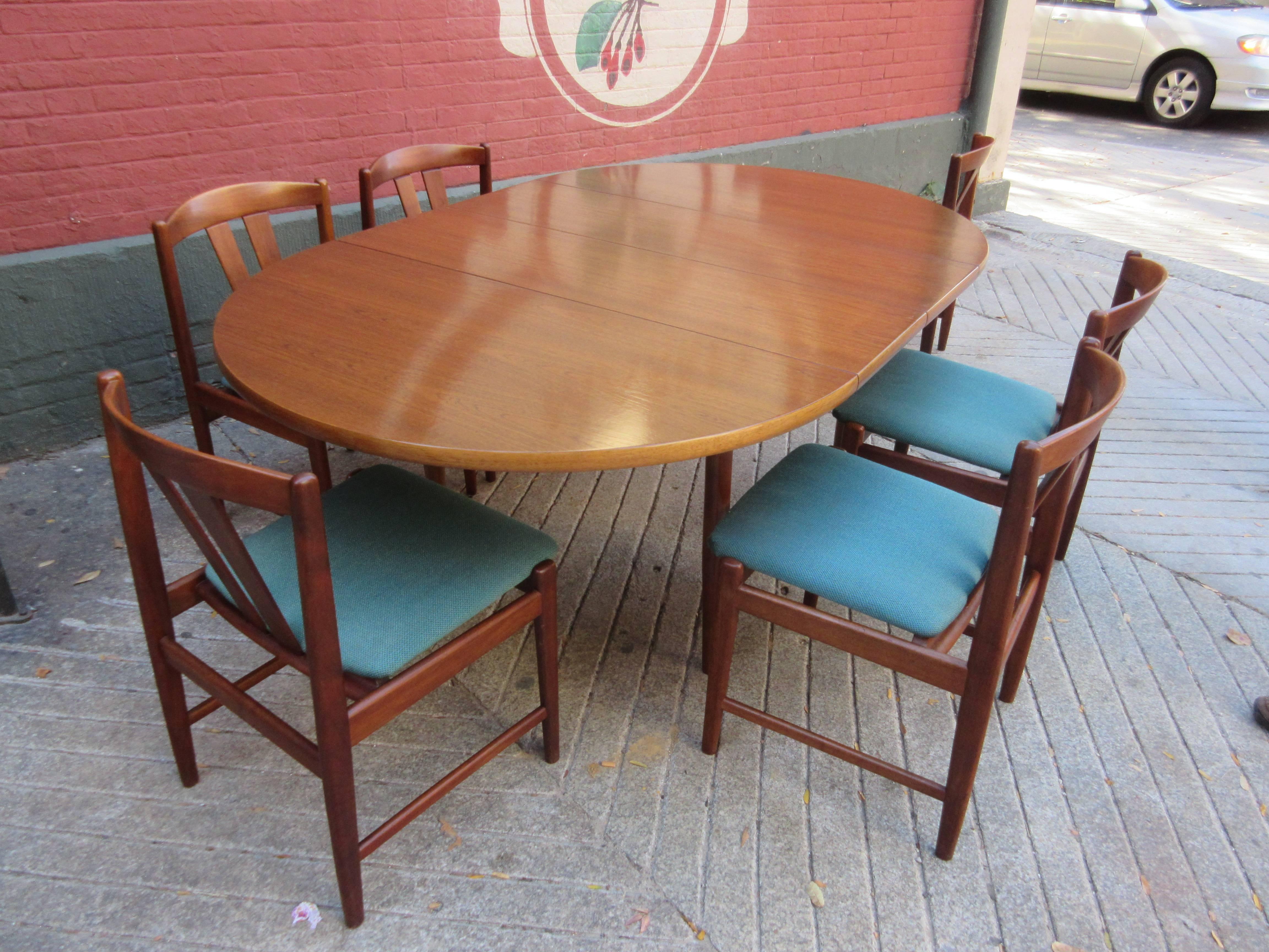 Teak table and chair set with labels on chairs and burnt brand on table. Round table extends to oval with two leaves. Original blue fabric lightly soiled and faded. 45 inches round with two 13 inch leafs making a 71 oval table. Chairs are 30.5