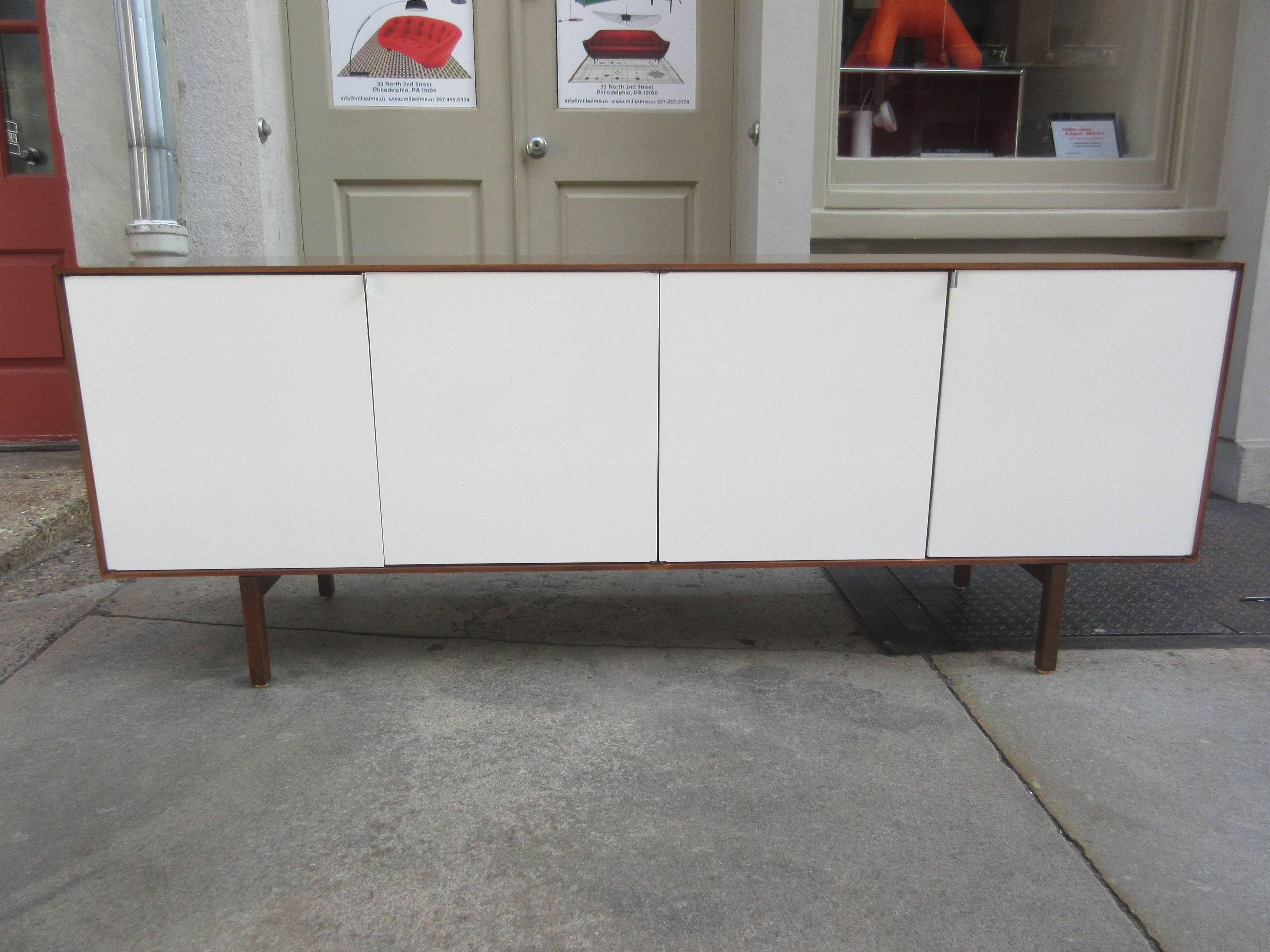 Lacquer fronted doors in cream give a lightness to this large credenza. Legs have beautiful mortised joints and interior reveals storage of adjustable shelves and drawers. Legs and cabinet are of walnut with chromed finger pulls one two of the four