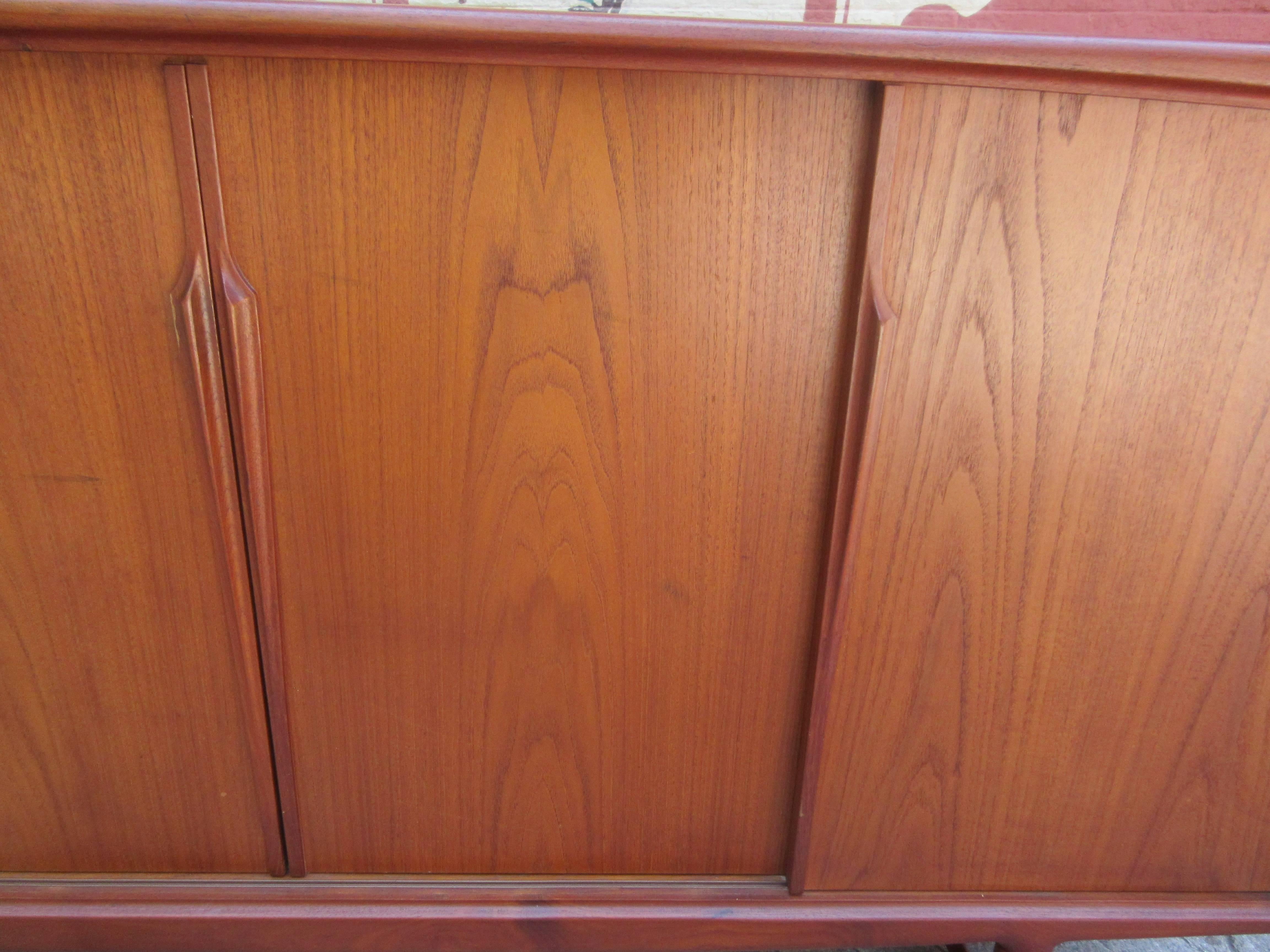 Large teak credenza from the 1960s with huge amount of storage. Four large sliding doors reveal openings of adjustable shelves and removable drawers line the interior. Cabinet is supported by four cylindrical legs joined by stretchers.