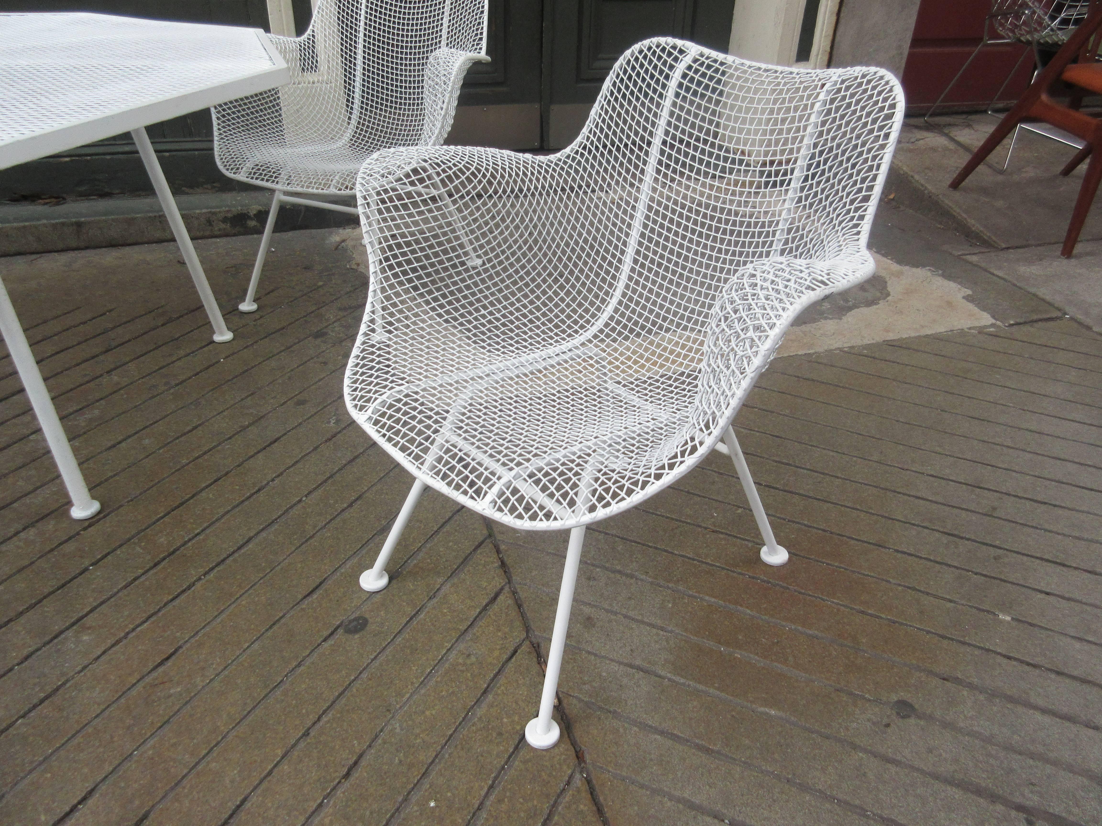 Table and four chairs of rolled, mesh, wrought and tubular steel by Woodard from the Sculptura Line. Hole in middle for outdoor umbrella.