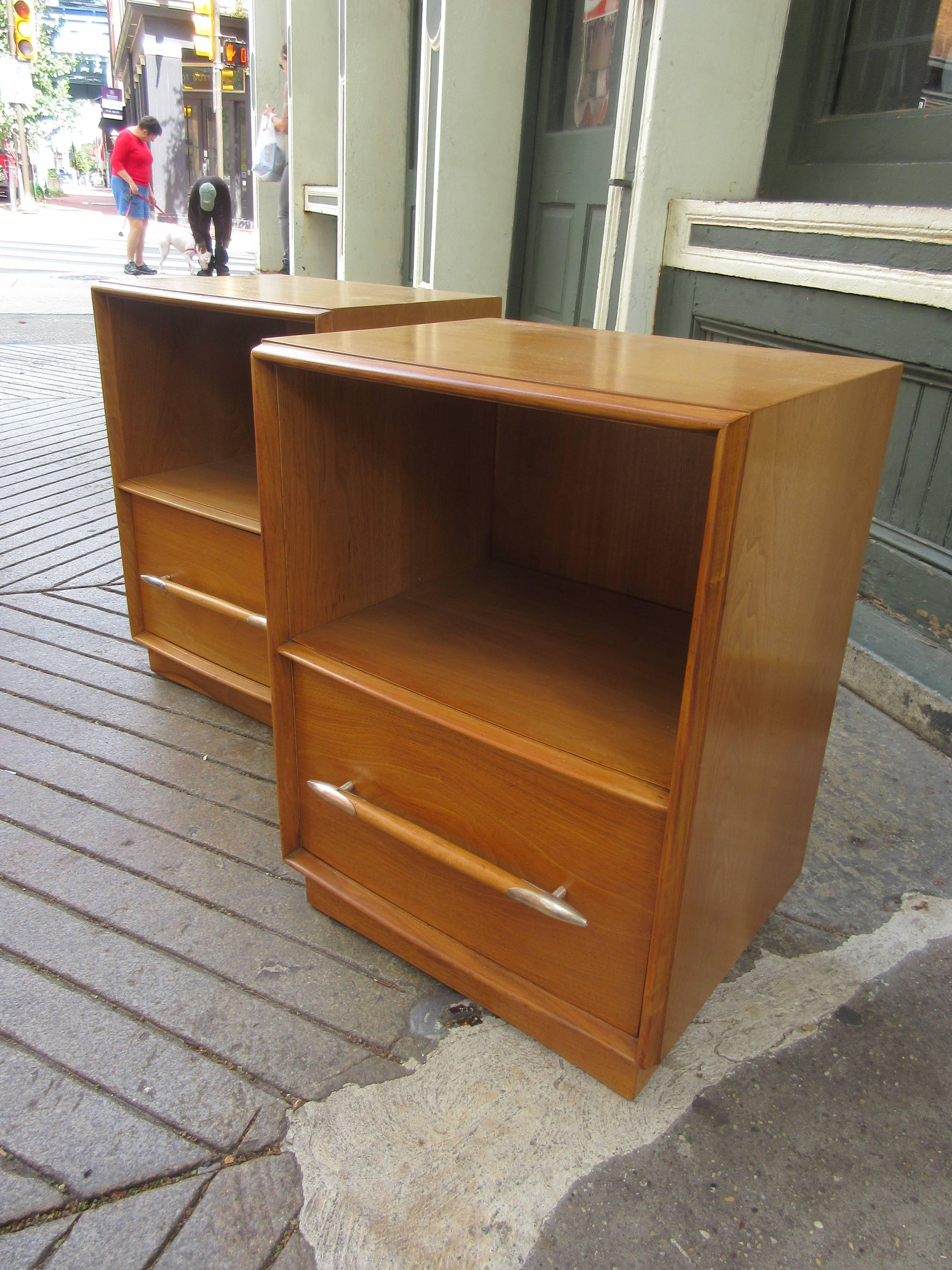 Pair of nightstands in honey walnut with polished aluminum drawer pulls. One large drawer at bottom of each with larger open space above. Pieces retain original tags. One is slightly lighter than the other but not noticeable when separated by a bed.