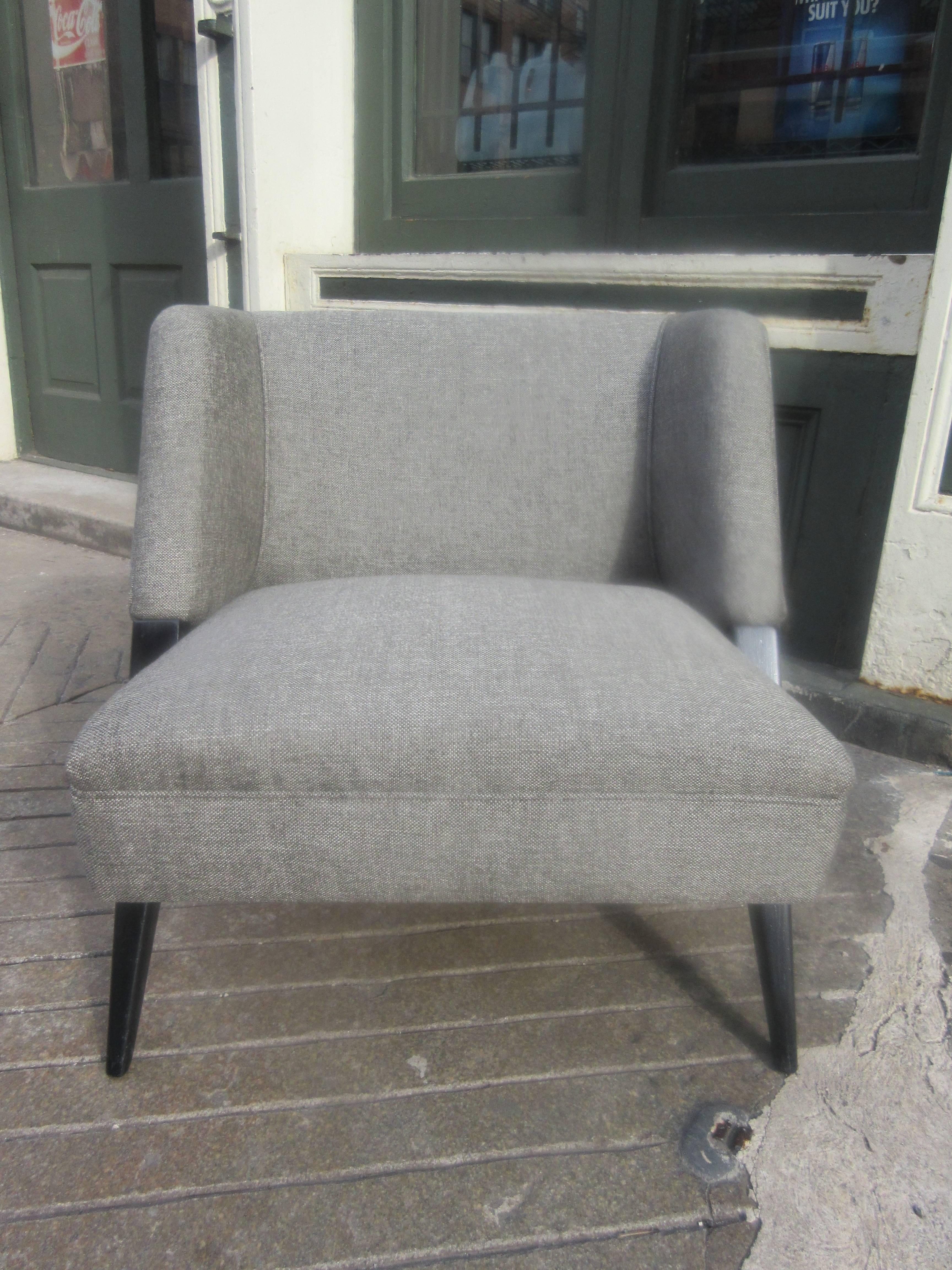 Armchair with a rakish angled leg which becomes part of the frame of the arms and back. Just redone in a medium gray hopsack weave fabric. Tapered legs are ebonized allowing the grain of the wood to show through.