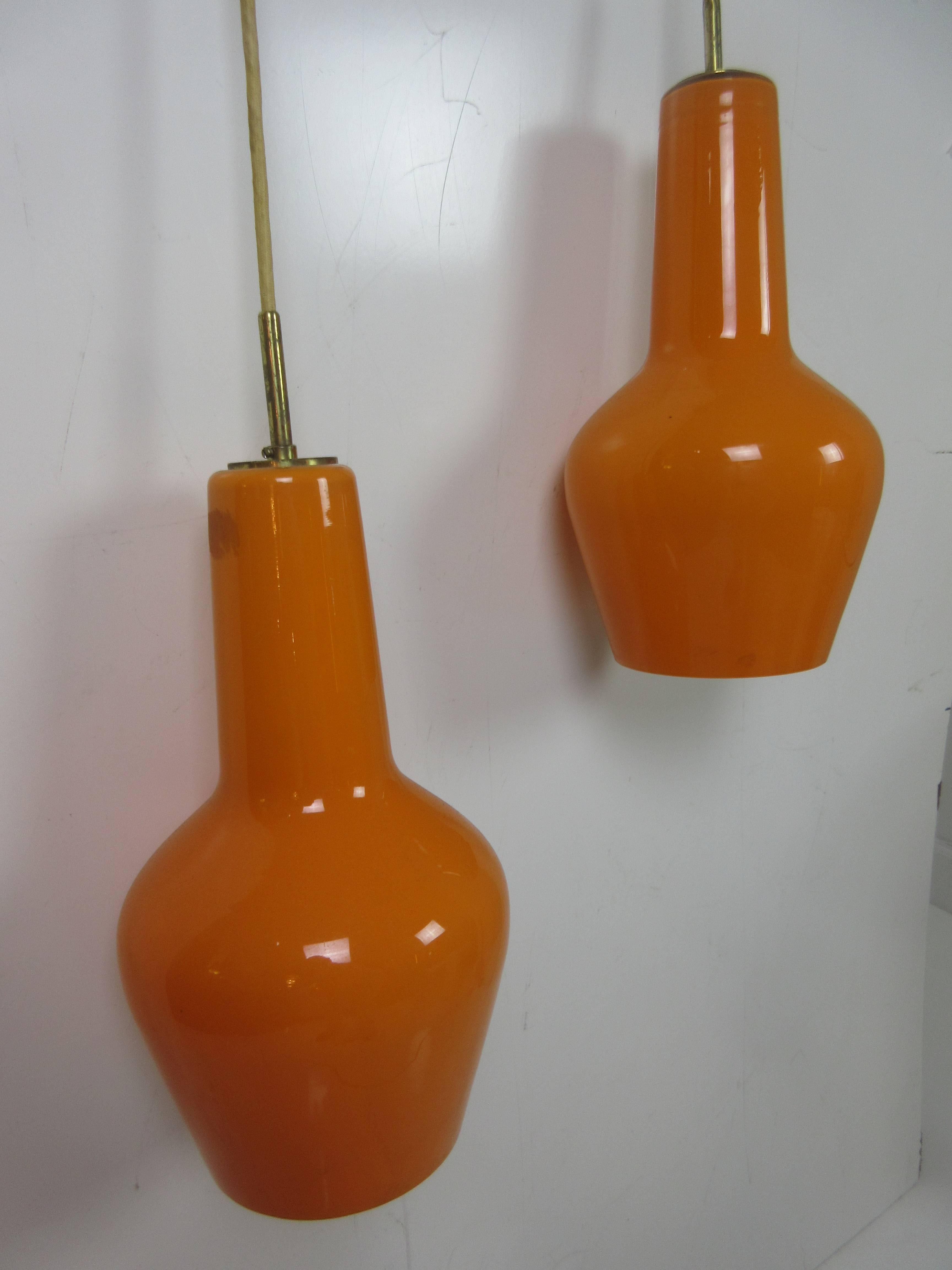 Danish cased orange glass pendant ceiling fixture from the 1950s. Brass fixture suspends and separates the two globes. Original cloth covered wire remains. Length of wire is adjustable for varying globe height (both globes the same position or