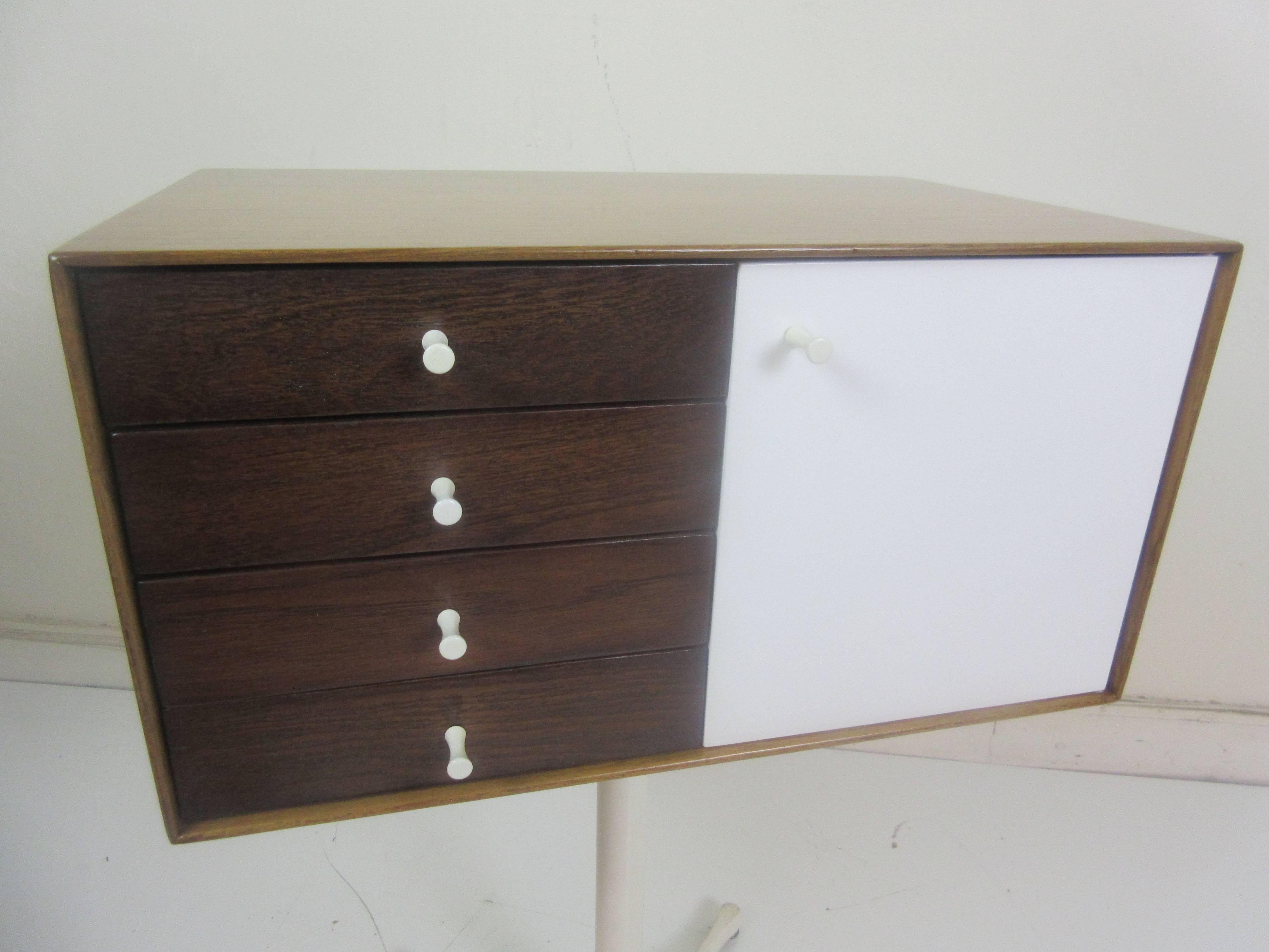 George Nelson miniature jewelry chest for Herman Miller on swag stand model 5211. This version is in teak on all sides with cream lacquered large door and rosewood drawers. All knobs in great original condition. Stamp on bottom identifies this as