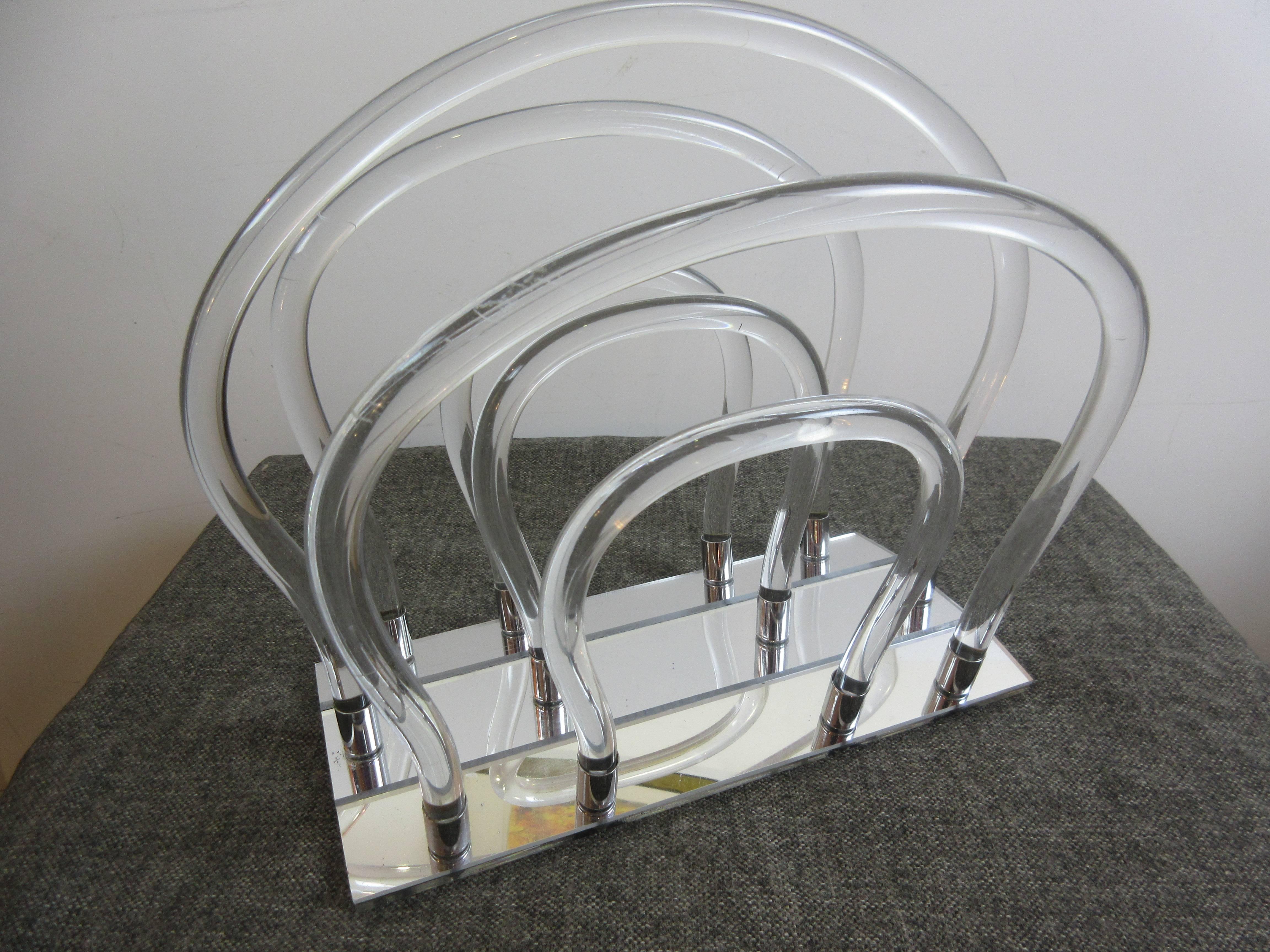 Classic 1970s Dorothy Thorpe magazine rack with mirrored bottom. Curvy round bands of Lucite that fit into round chrome holders that are mounted to the mirrored base.