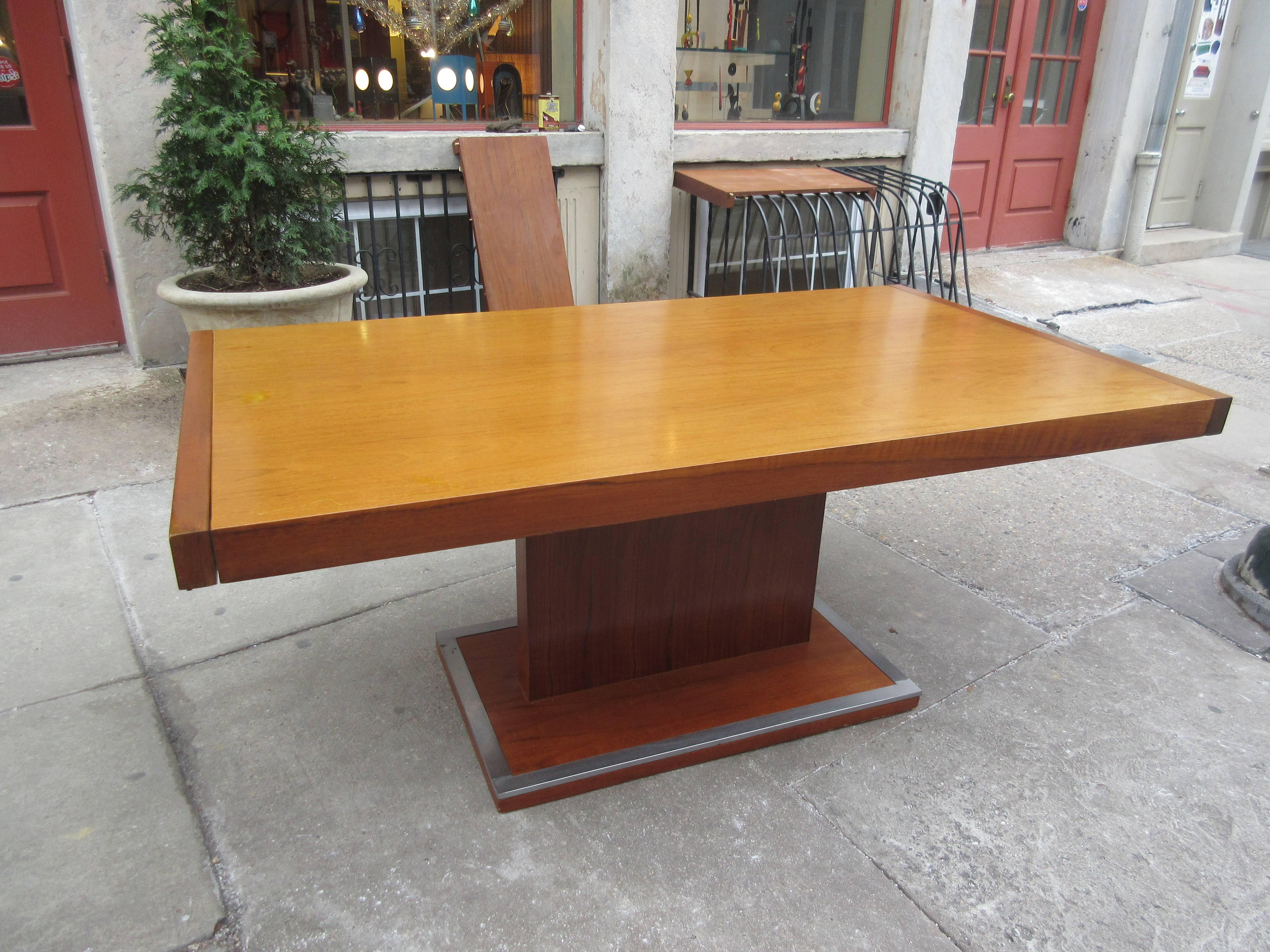 Founders dining table by Milo Baughman in two shades of walnut with aluminium trim on pedestal base, centre pedestal and top are in a warm honey walnut and are capped on either end by a slightly darker walnut leaves by cantilevered pull-out