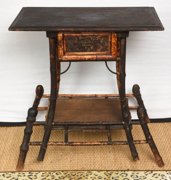 Rare French bamboo and rattan table circa 1860-1870 has decorative leather drawer with raised motif which opens on either side, decorative metal handles both sides. Bamboo legs and frame work shades from amber tiger coloring to deeper brown/black.