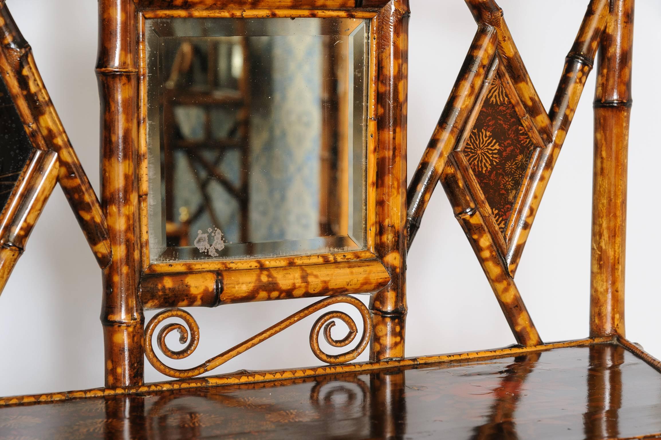 A nice English lacquer bamboo cabinet or bookcase, the pierced back inset with a beveled square mirror flanked by lacquered panels, the lacquered trapezoidal top with a glazed door opening to a shelved interior, over a medial shelf on sabre legs.