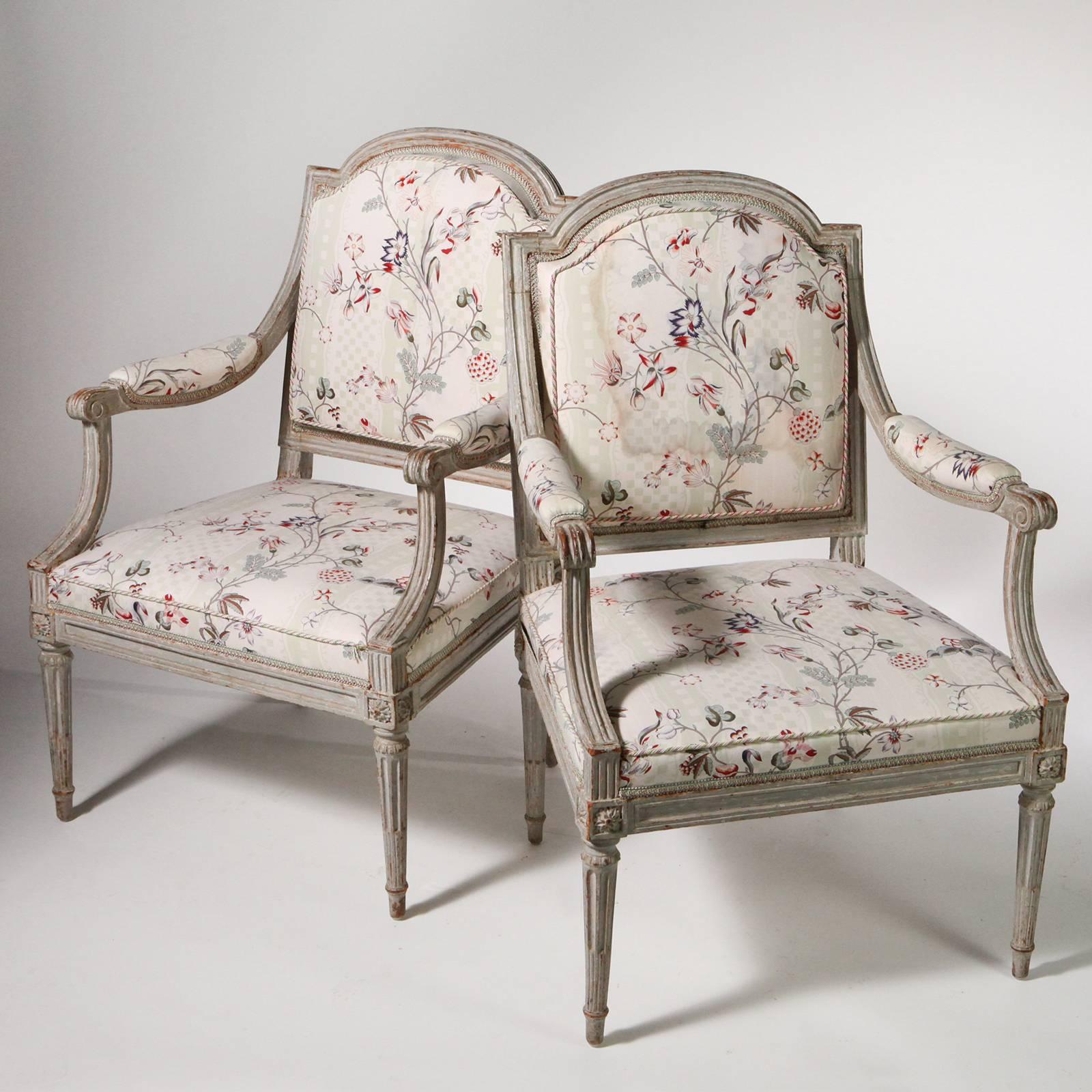 Pair of French 18th century fauteuil chairs. Painted gray wood frames with gracefully shaped backs, square seats, upholstered arms and reed legs. Upholstered in an elegant light floral fabric on cream background. Comes with separate plump seat