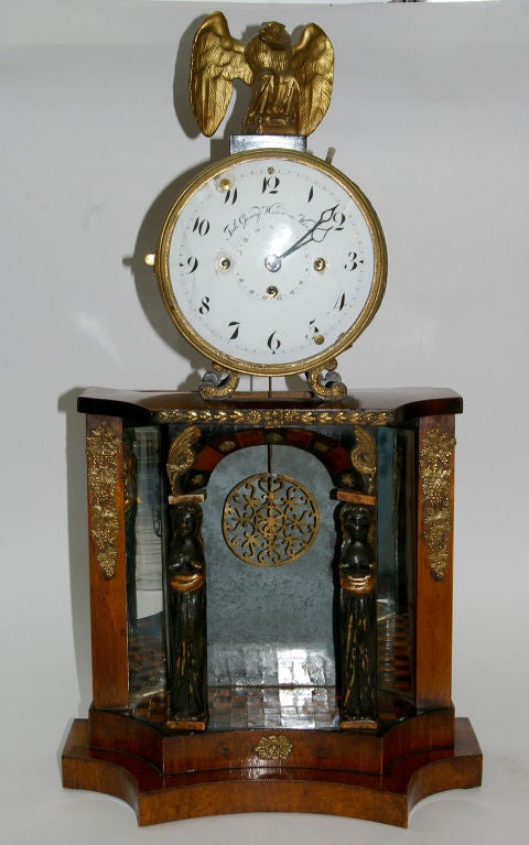 This handsome working clock is an example of the Biedermeier period, c1830. It has the classical elements of Caryatid columns on a stage of inlaid tiles. The backdrop is a patinated mirror showing off the pierced brass pendulum on a stage like