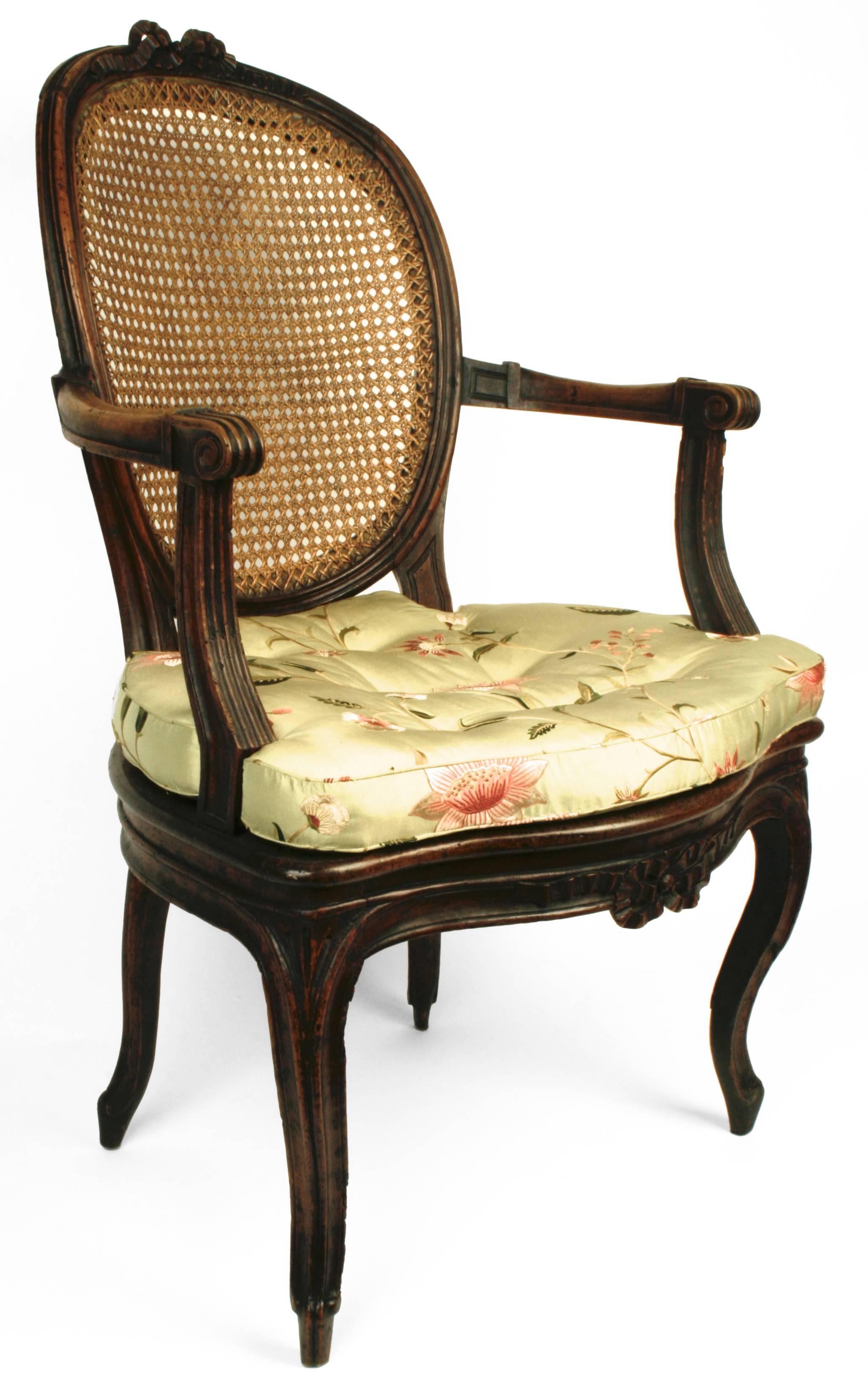 This very pretty armchair is made of walnut. It is open carved with bows centered on the crest rail and a matching one on the apron. It has soft scrolled arms and curving cabriolet legs. Both the oval back and the seat are caned with a custom