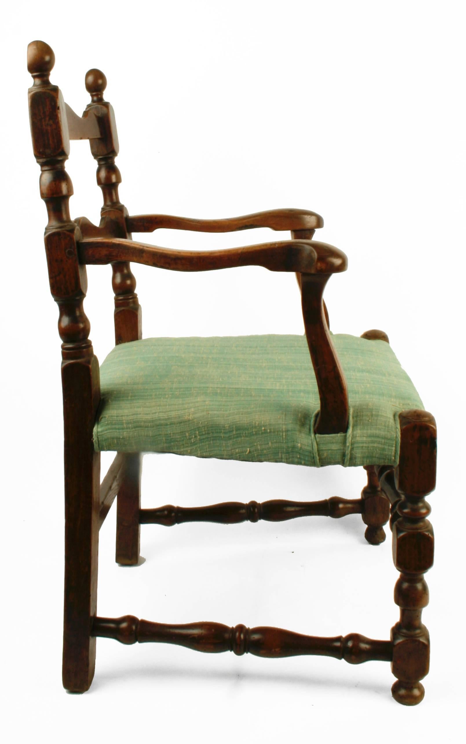 This handsome French armchair is made of Walnut with an upholstered seat and open back. It has turned uprights, front legs and stretchers. The uprights are topped with flat back finials. The back rails are scalloped with soft curving arms. A green