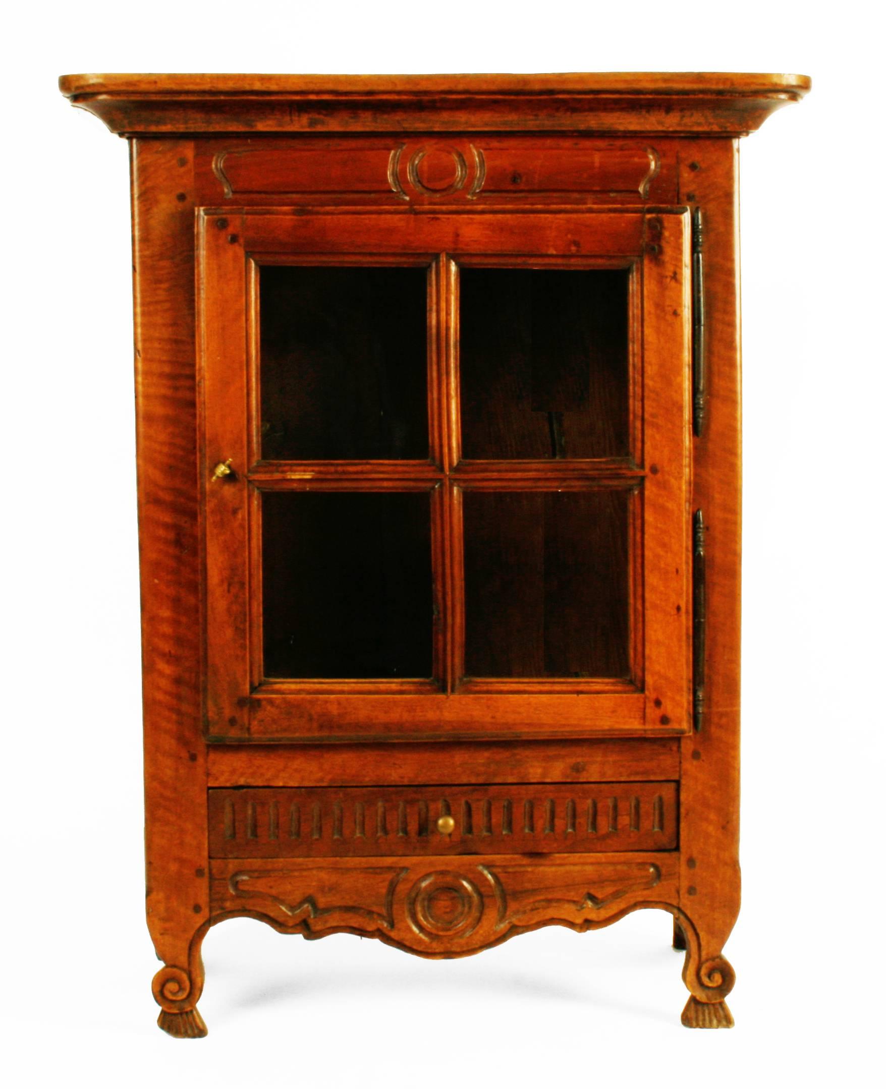 This handsome French display cabinet is made of carved walnut. It has a single drawer and a scalloped and carved apron. The four paned glass door opens and latches with a grasping fist shaped brass latch. It stands on carved and scrolled cabriole