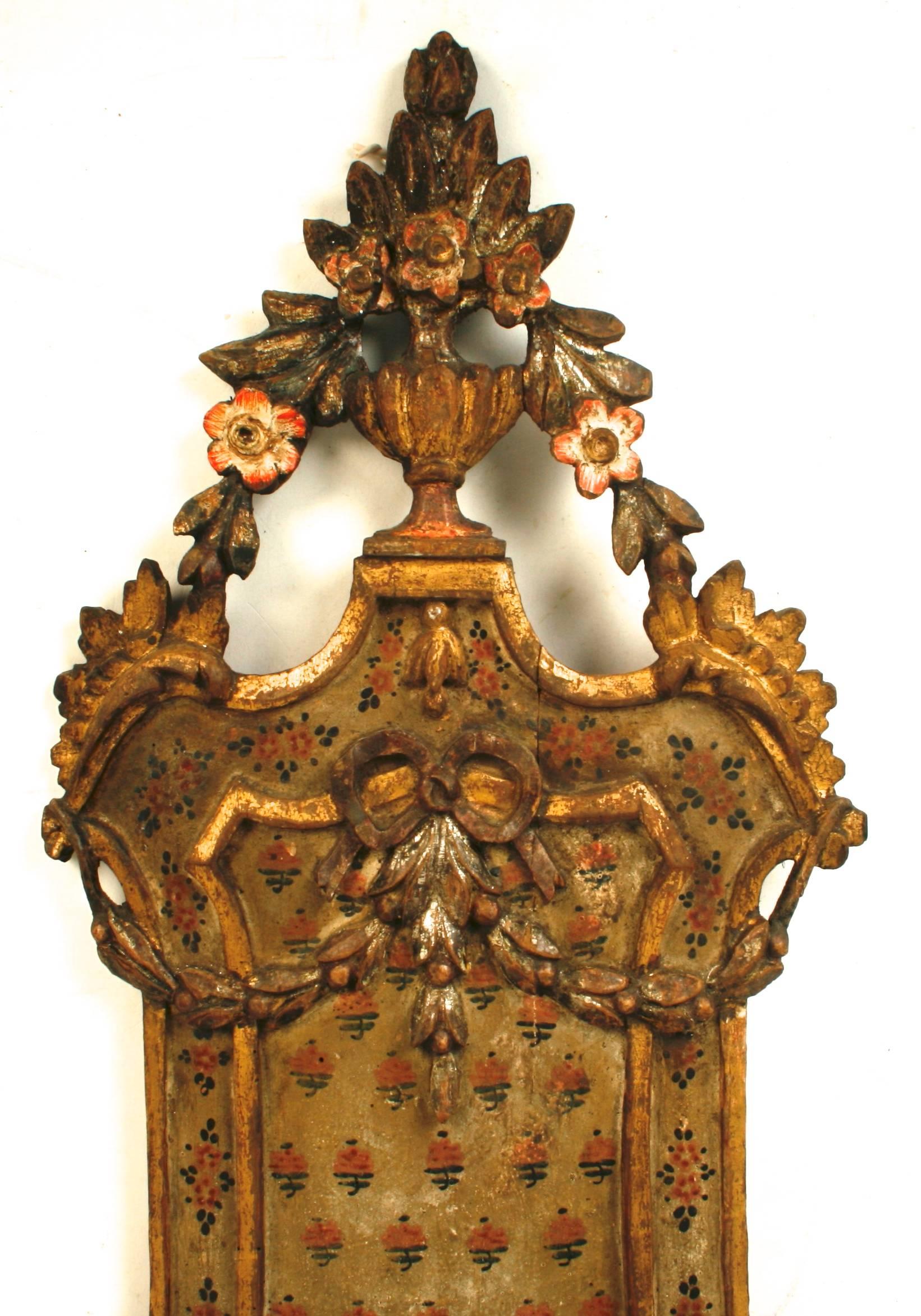 This ornate Italian carved and gilt wall shelf is decorated with hand-painted flowers and has scrolled trim, swags with a bow and is topped with a neoclassical urn. The shelf is trimmed with a scalloped apron and is supported by a scrolled bracket.