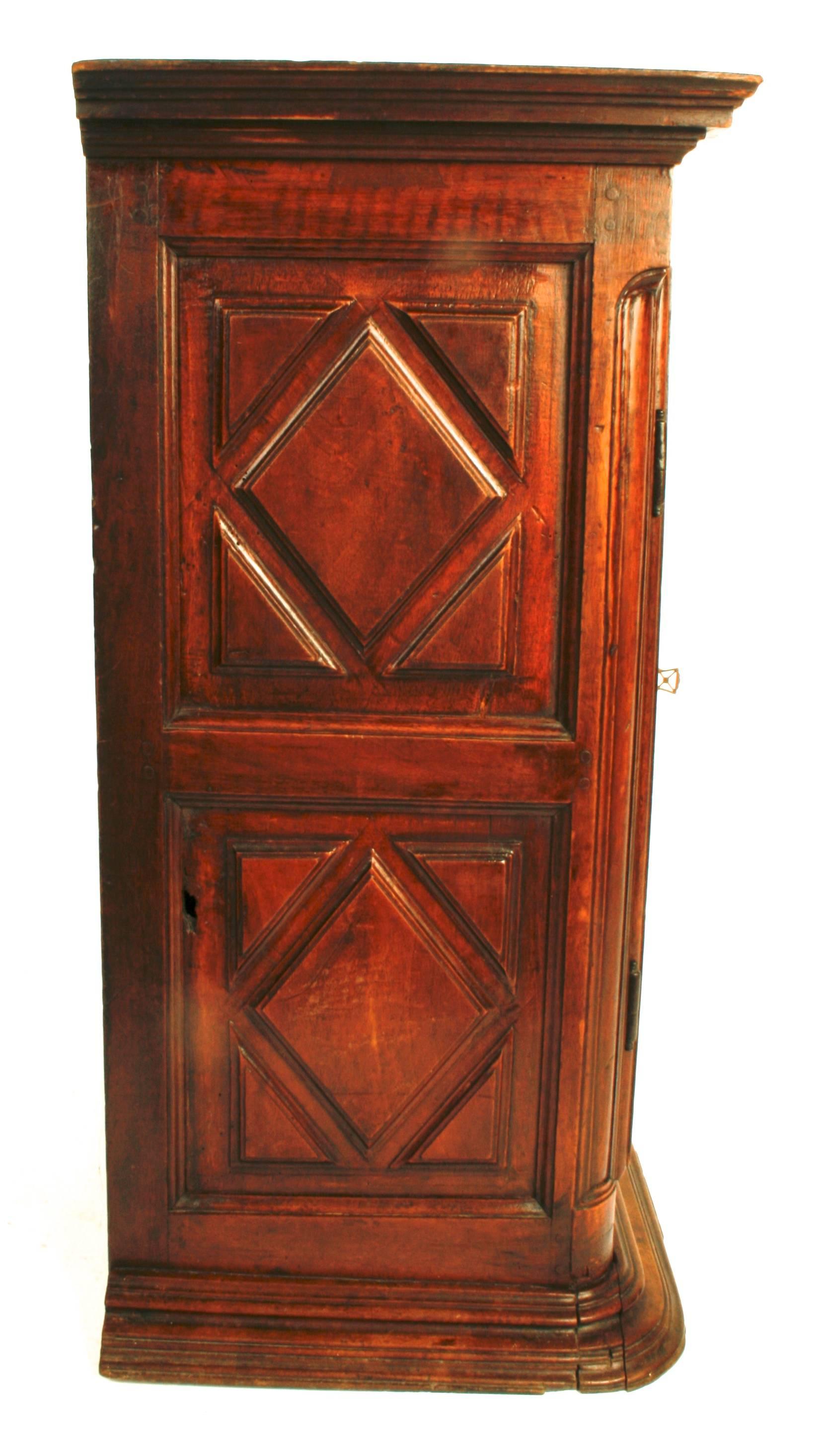 This handsome French wall cabinet is made of carved walnut. It has two carved doors with inlaid stars and original brass hardware with locking key. It has one interior shelf with a brass hook latch and two small drawers with brass knobs. The front