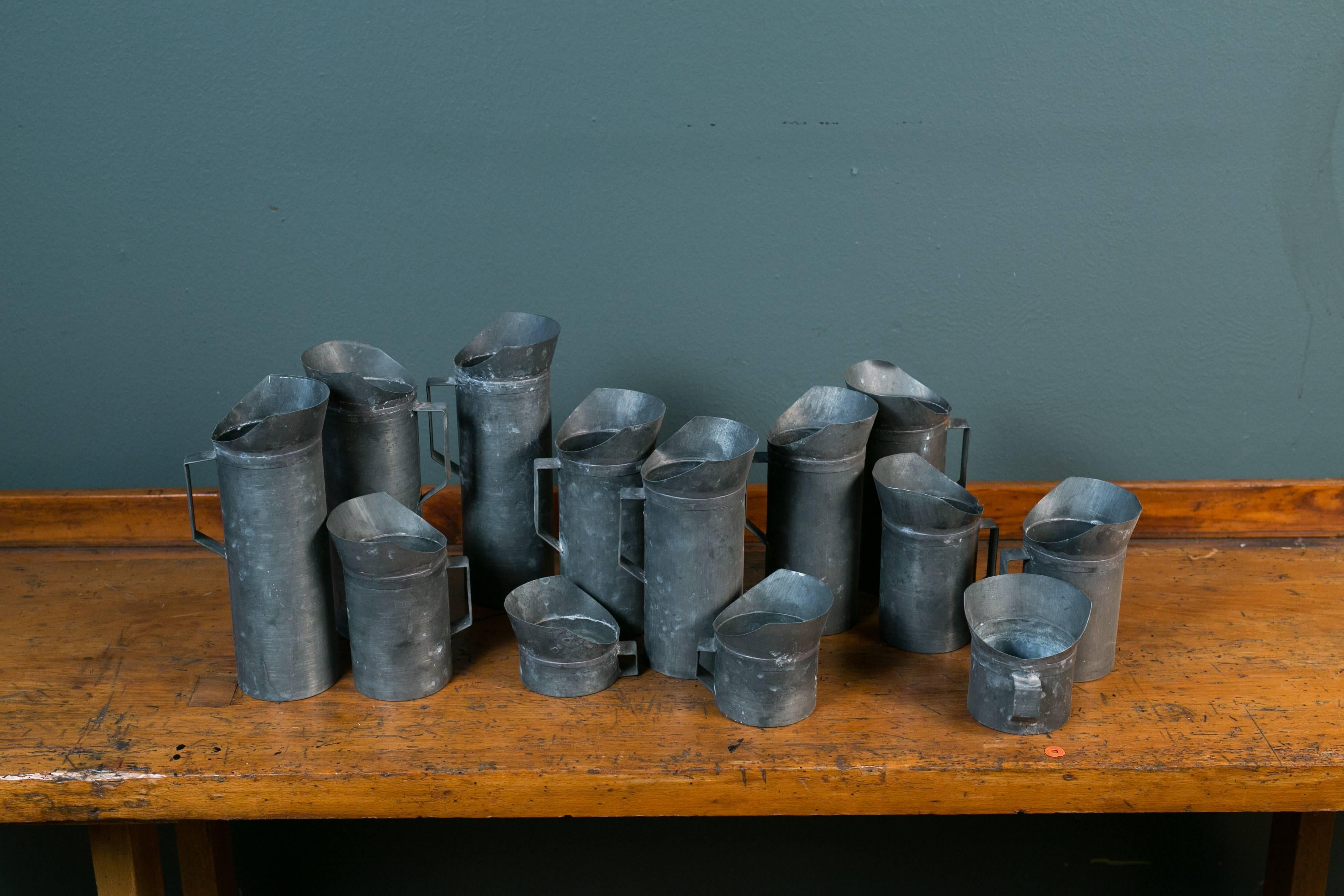 Collection of 13 zinc measures or pitchers, handmade in France, circa 1940s. Shortest measures 3.75 inches W x 4.25 inches D x 2.75 inches h. Measurement listed is of tallest ones. Not guaranteed to be water tight- some appear to be, some don't.