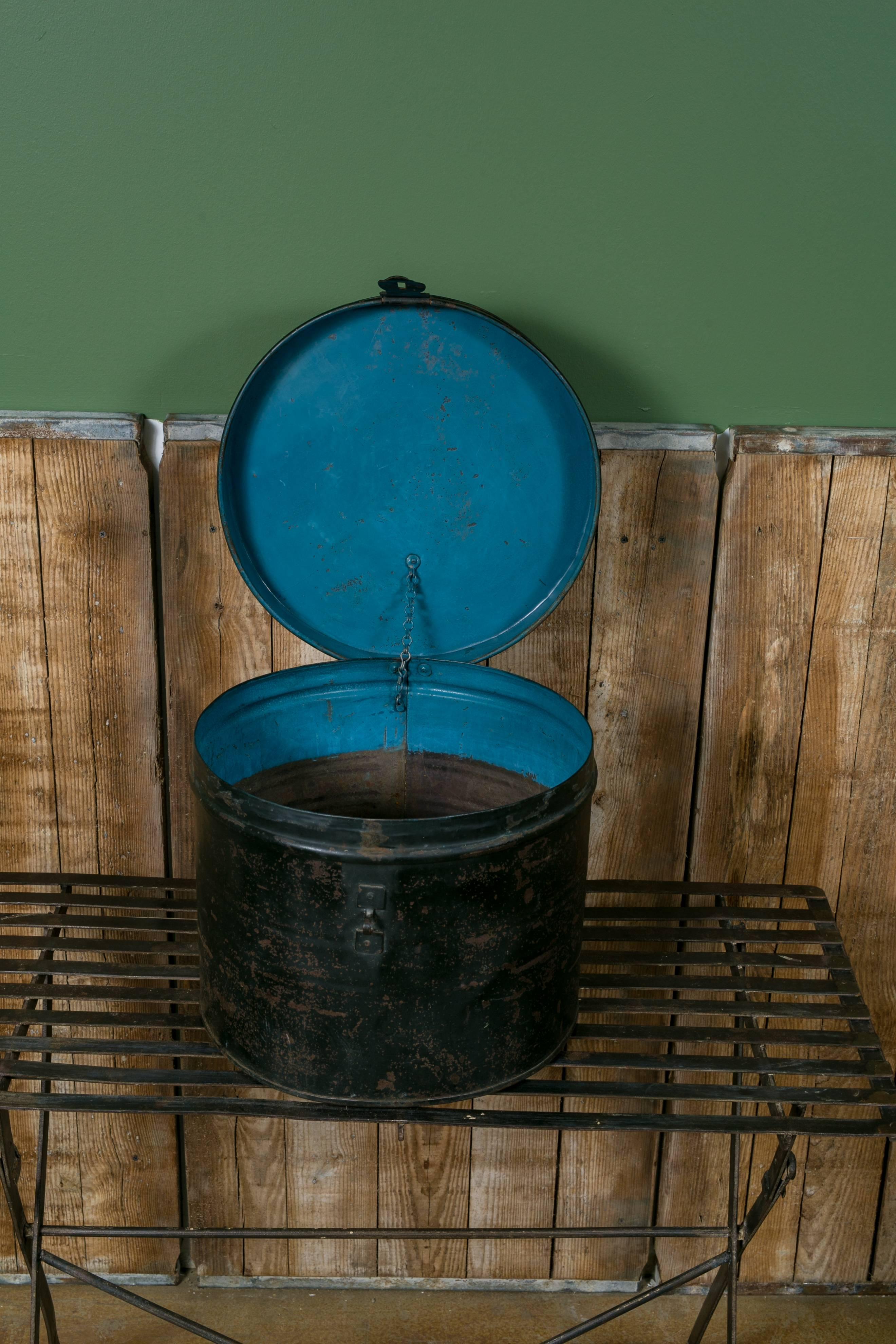 Hinging metal hat box from J. Delsart, Belgium, circa 1920. Black painted exterior with bright blue interior lid and banding. Original stamped metal plaque on the front above the metal hinge with chain on interior.