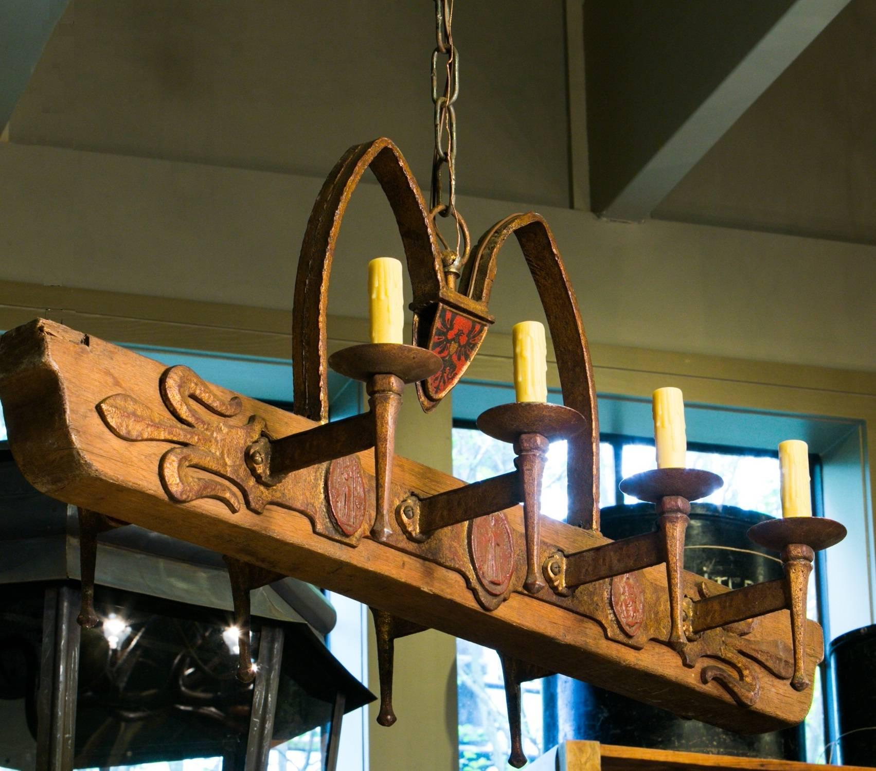 Wonderful and heavy, handcrafted wood and iron chandelier from Spain, circa 1940. Painted metal shield at the top has a stylized coat of arms heraldry look to it. Red and black winged animal on one side, green and gold on the other side. Medallions