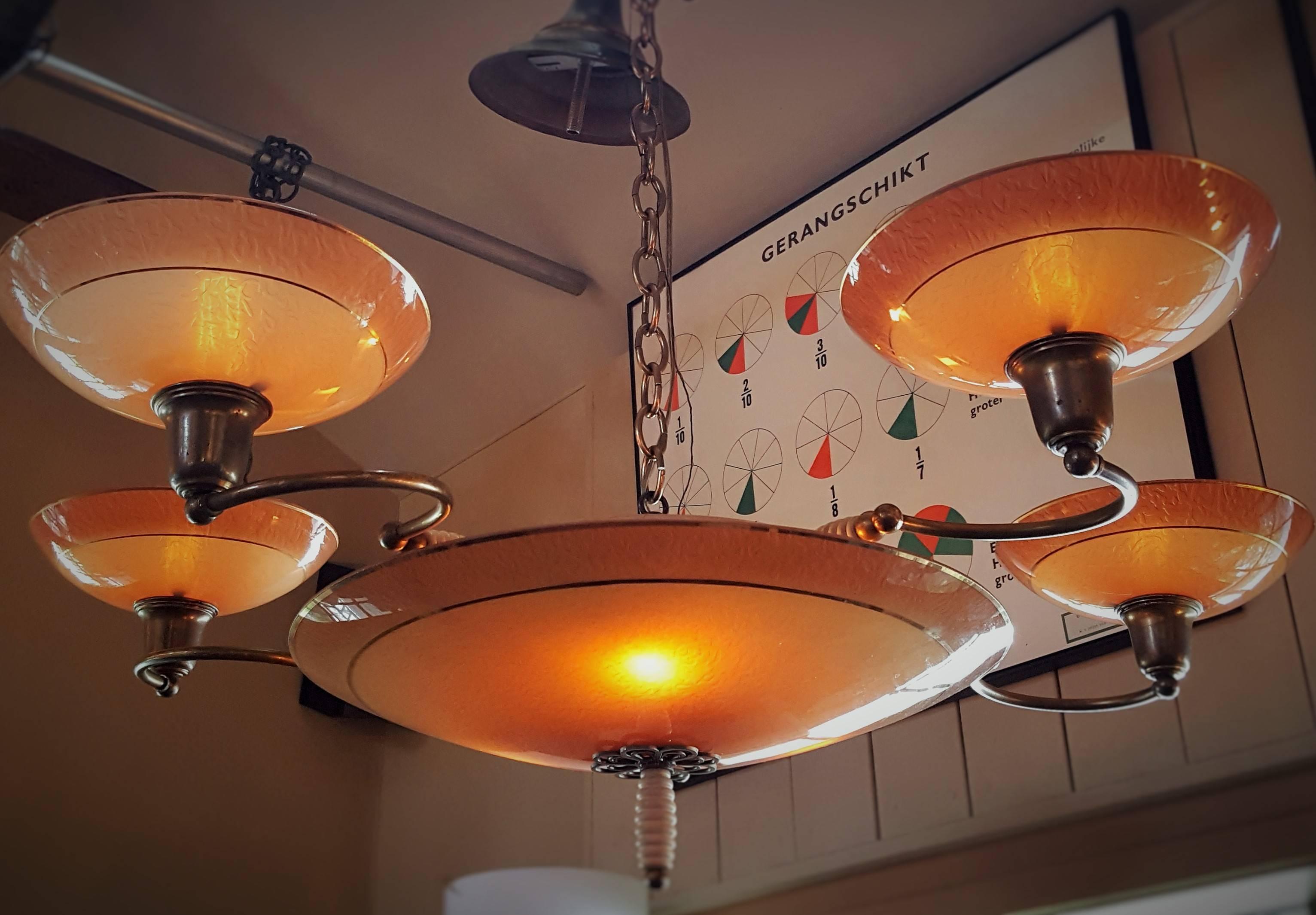Unusual eight-light chandelier with apricot- salmon colored textured glass and gold accents. From France, circa 1940. Brass arms and detailing with a white wood twist finial at the base and on the arms. Comes with brass chain and canopy. Newly