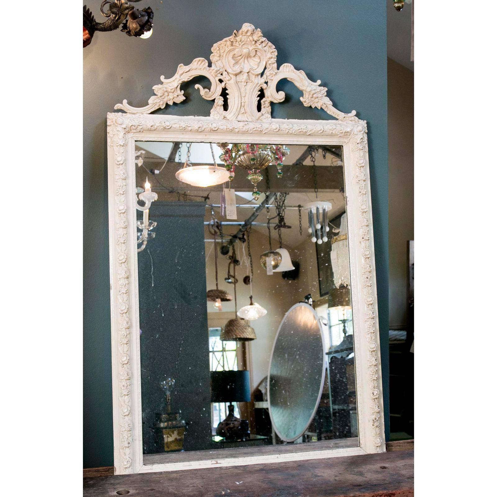 Beautiful, large antique Rococo-style French mirror with floral motif, circa 1900. Carved tassels line the base of the mirror and a stylized seashell rests in the apex, flanked by swags of flowers. Original paint in a creamy white lacquer over wood