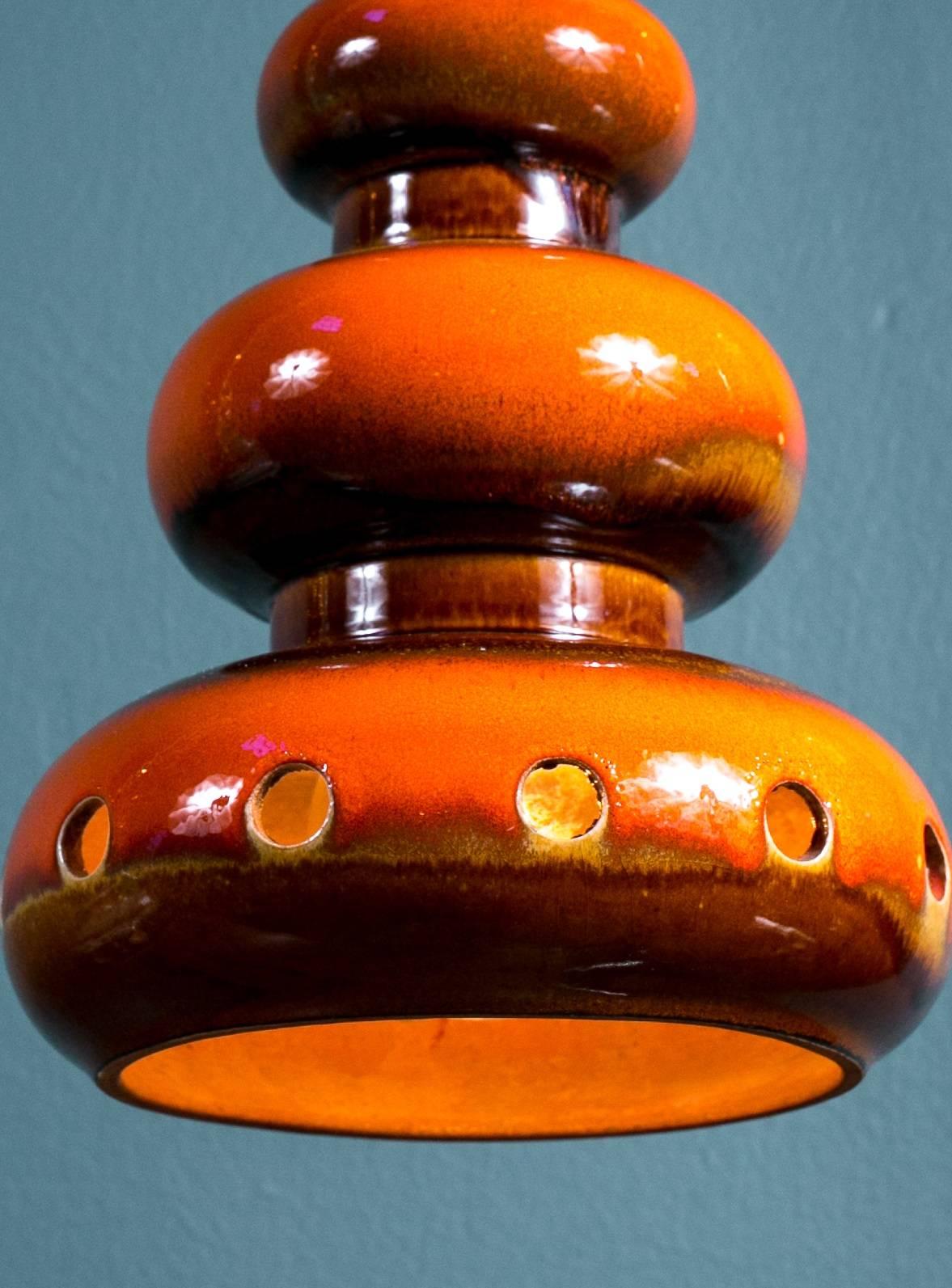 Handmade ceramic glazed pendant with cut-out circles at the base. Interesting glazing with the orange color blending into gold and brown. Natural terracotta coloring inside. Newly wired for use in the USA with all UL listed parts, a porcelain Edison