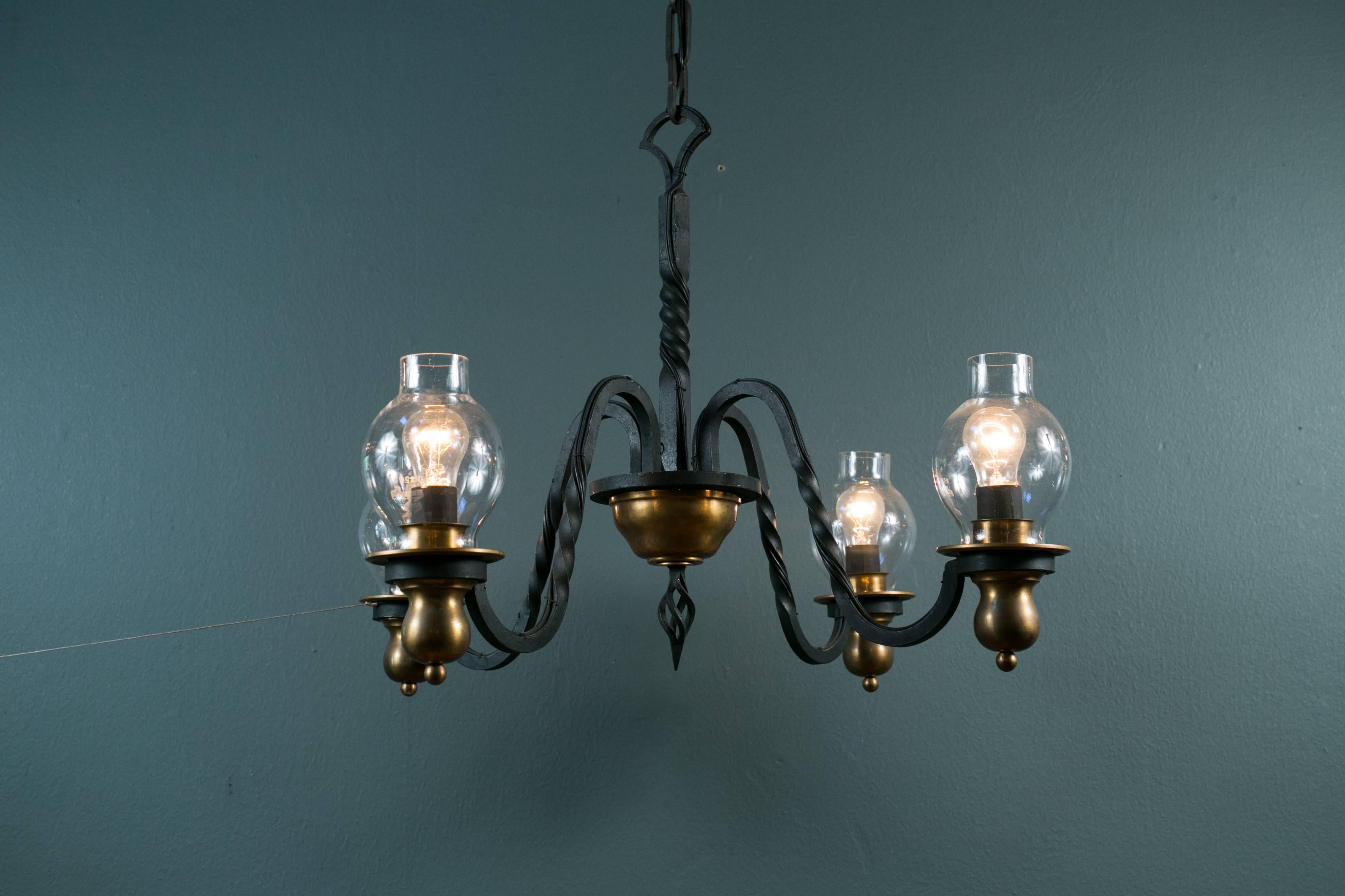 This unusual fer forge' brass and wrought iron light is in the style of Gilbert Poillerat with vintage glass hurricanes. Newly wired in the US with all UL approved parts and four Edison sockets-maximum 60 watts each. Measurement is to the top of the