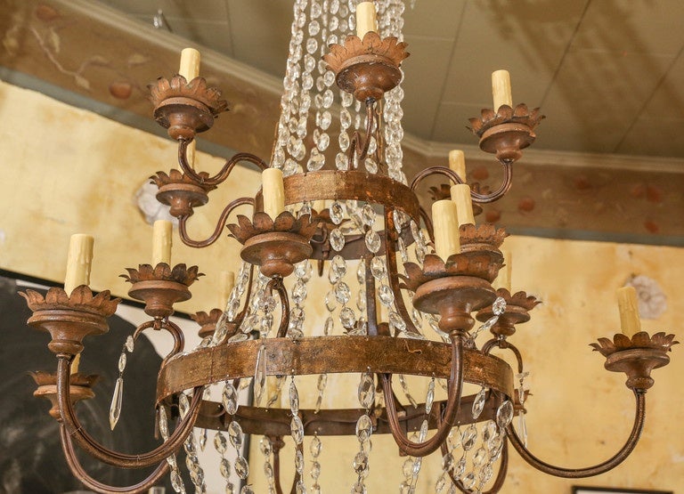 Large gilt-iron Italian chandelier (early 19th century) from Lucca. Decorated in pendants and chains of crystal prisms. Eighteen arms each support a gilded tole and carved wood bobeches cup, newly-wired with a medium-size light. Includes extra chain
