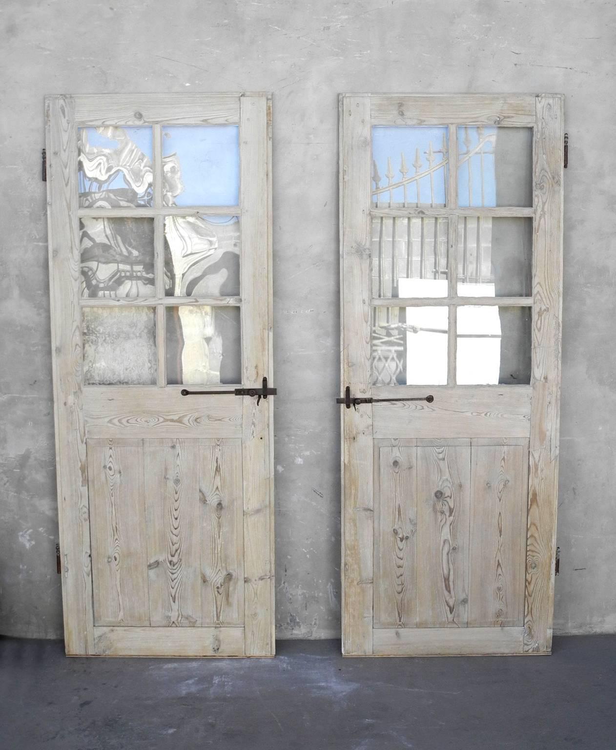 This is an identical set of two antique early 18th century glass doors from a "Maison Bourgeoisie" in Lyon, France. They have been stripped of color, so their wood is natural. They have identical antique hardware that boasts an adorable