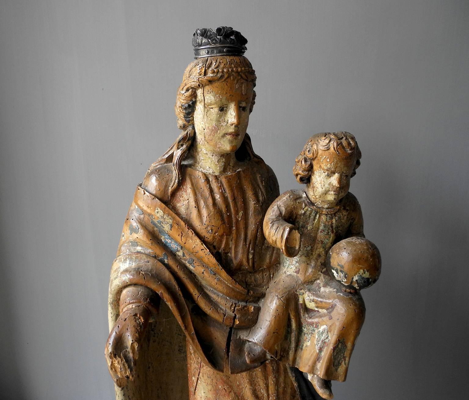 This 17th century painted wooden virgin was found in Italy. It includes its original paint and has somewhat of a patina due to its age. The virgin has a metal crown atop her head and she is holding a baby. It is a perfect size for a historic antique