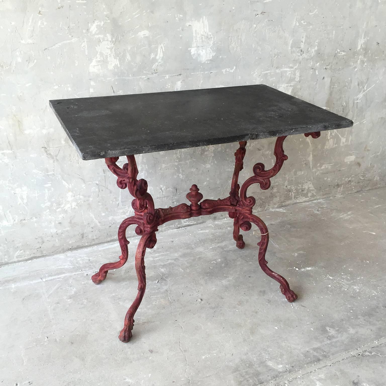 This is a charming antique table de jardin from the 19th century. This little table boasts a gorgeously intricate red iron base and a slate top. It is wonderful for a quaint al fresco patio or as a wonderfully European entry table.