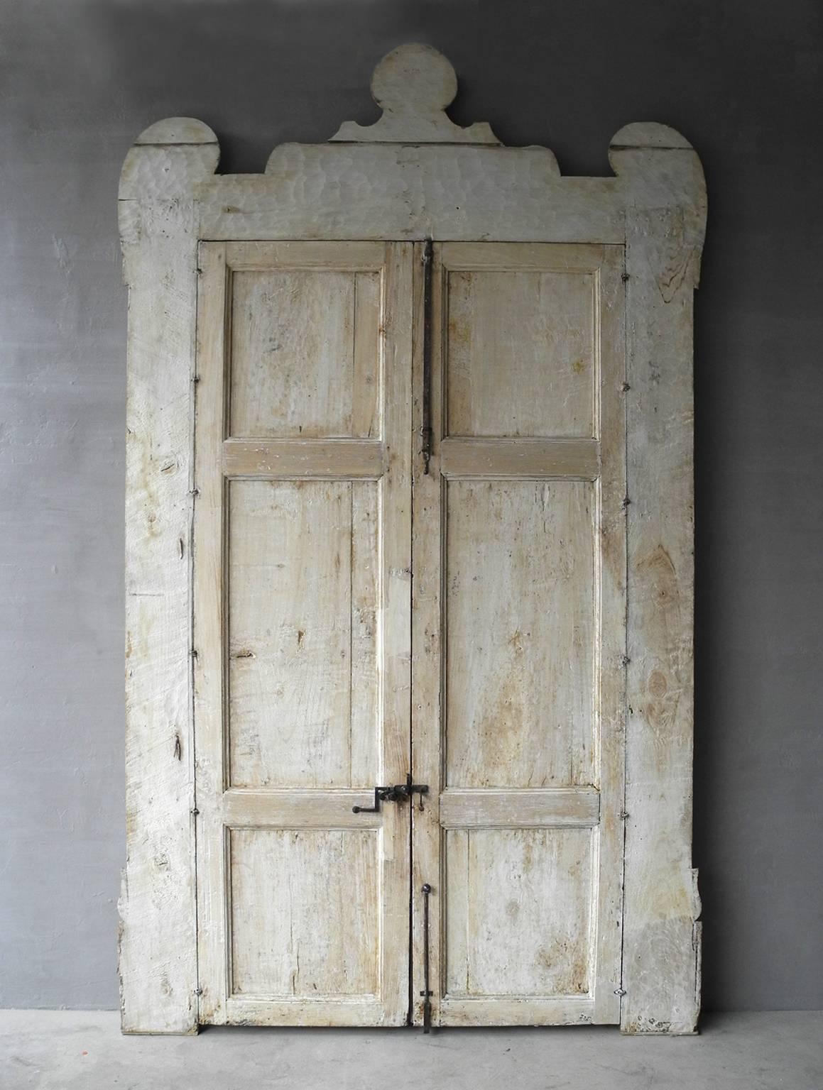 This is a very grand and large antique pair of white wood doors. They're extravagance comes from not only their carved face, but also their crown like frame that sits generously on top. They include antique hardware, from 18th century Naples.