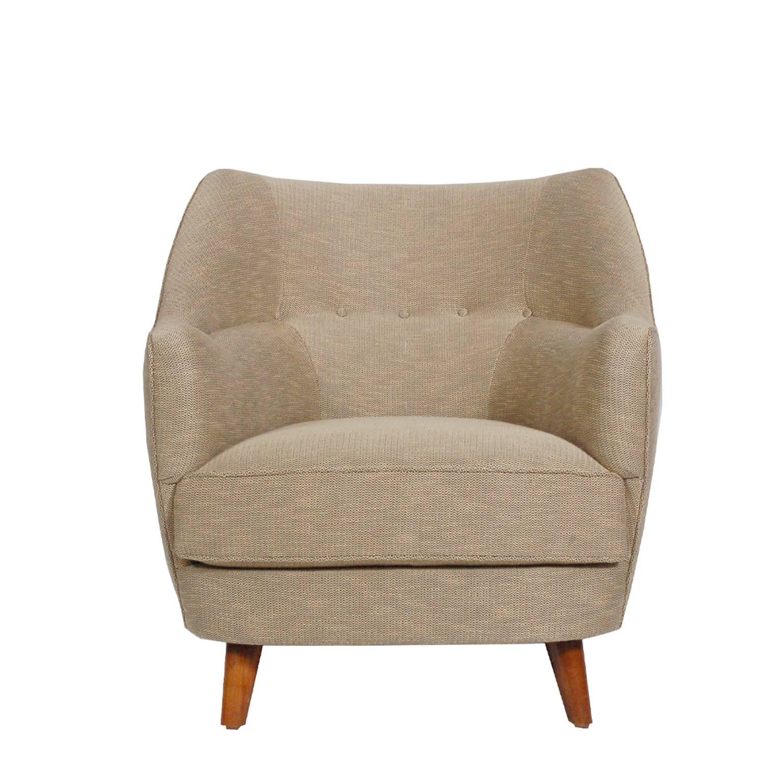 Rounded lounge chair with curving arms, inset seat and stained birch legs. Buttoned back and arms. Newly upholstered in coraggio fabric. Retains label from latex company, dated 1955.