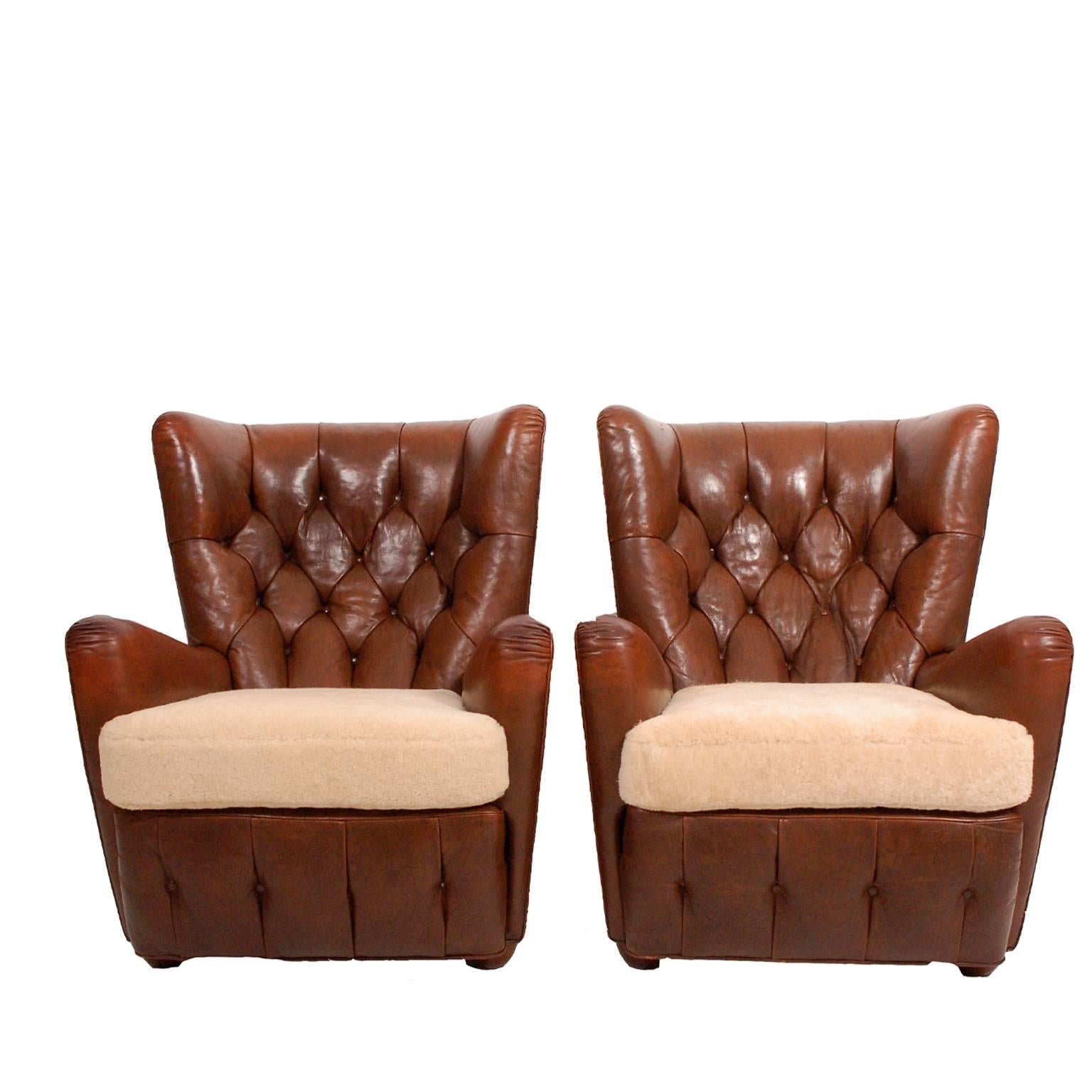 1930s Chesterfield style high back leather easy chairs with button back and base, sheepskin seats and original brown leather. Brass nailhead trim to both. Sitting on beechwood feet. Sold as a pair only.
