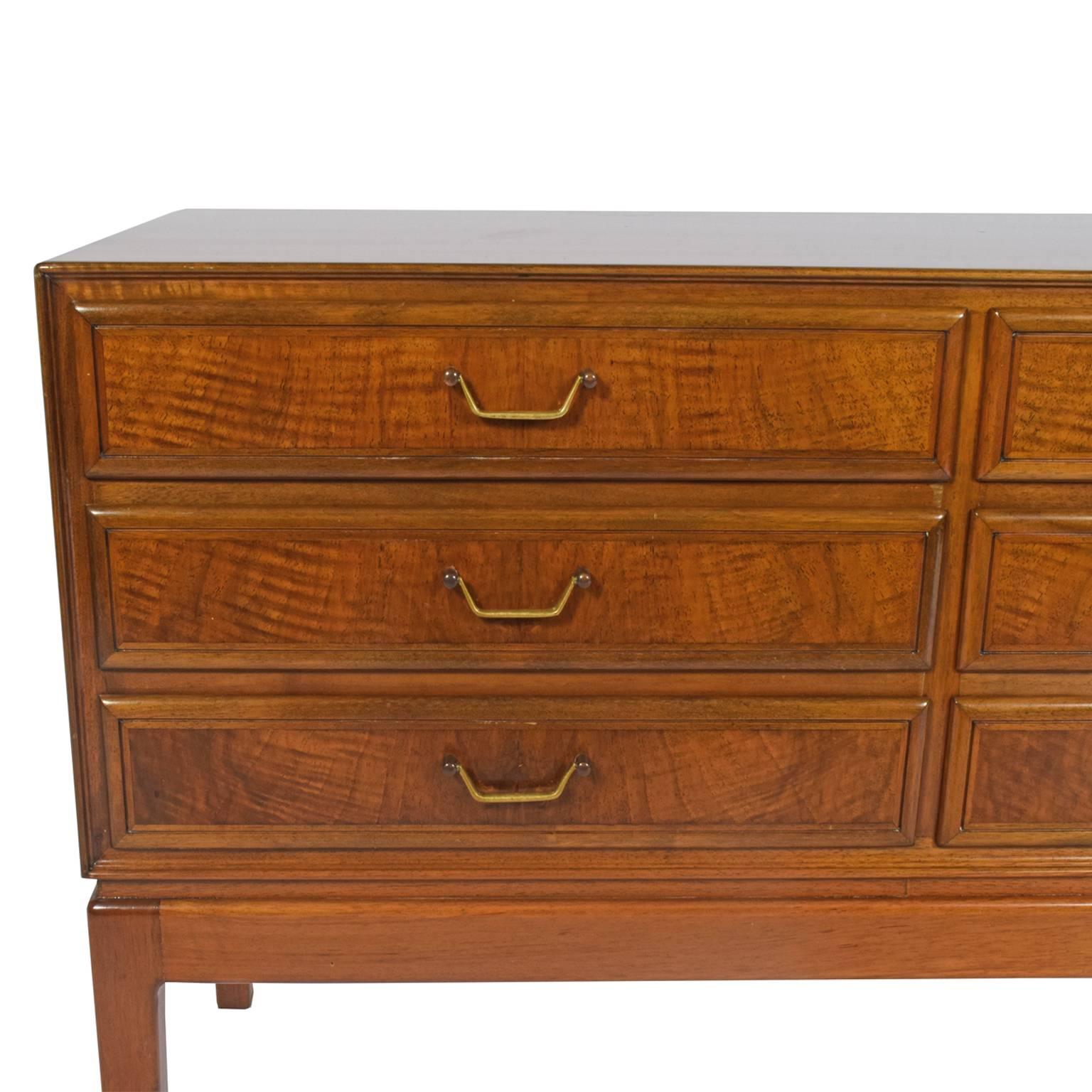 Six-drawer chest in walnut with brass pulls raised on solid walnut frame.