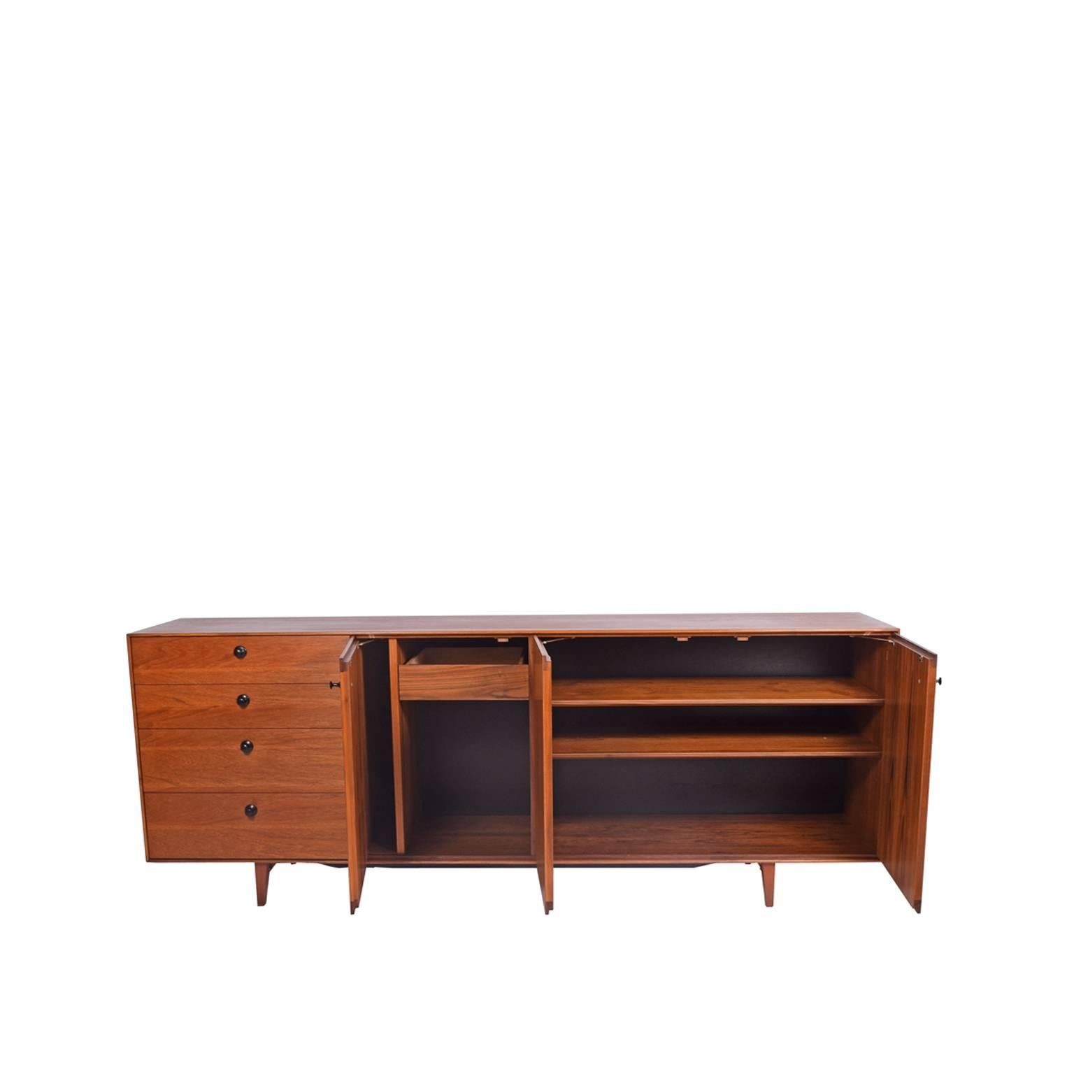 Cabinet features four drawers and three doors concealing two adjustable shelves, one drawer and open storage on solid teak legs with black pulls.