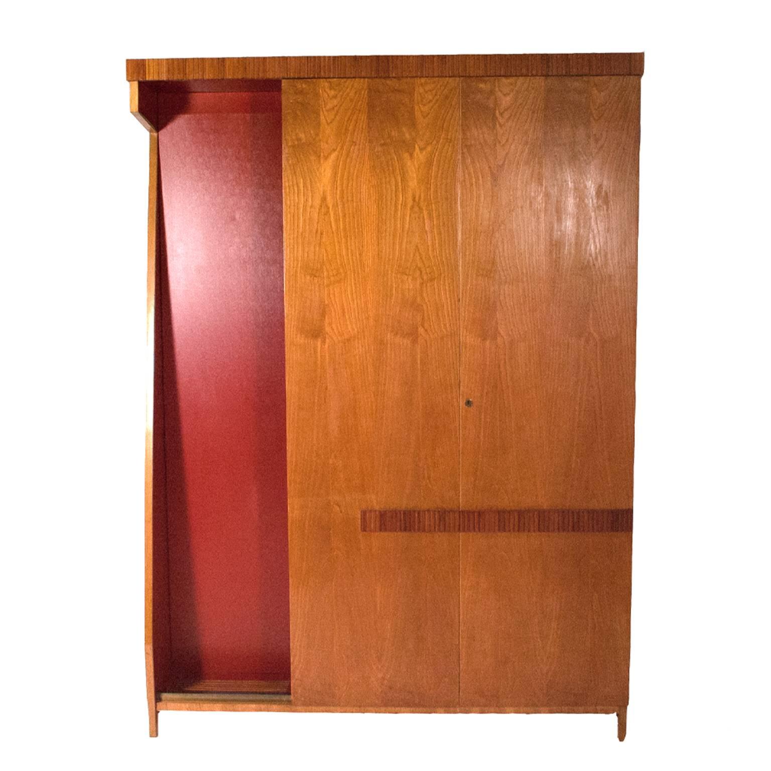 Large wardrobe made of ashwood with two doors in front that reveal small drawers, half door on side of wardrobe which opens to show shelves and tie rack. With red vinyl design element.