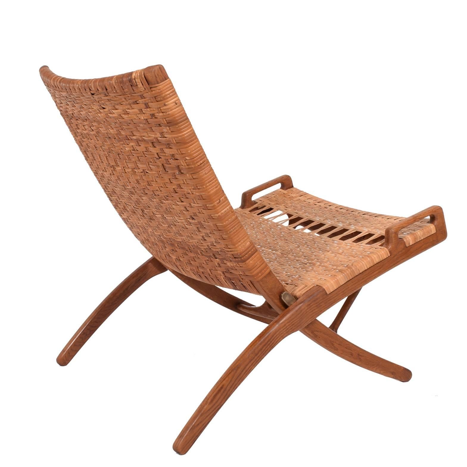Solid oak and flat-weave cane folding chair with a handle on each side and notched stretcher for hanging. Made by and burn mark signed by Johannes Hansen. Designed 1949.