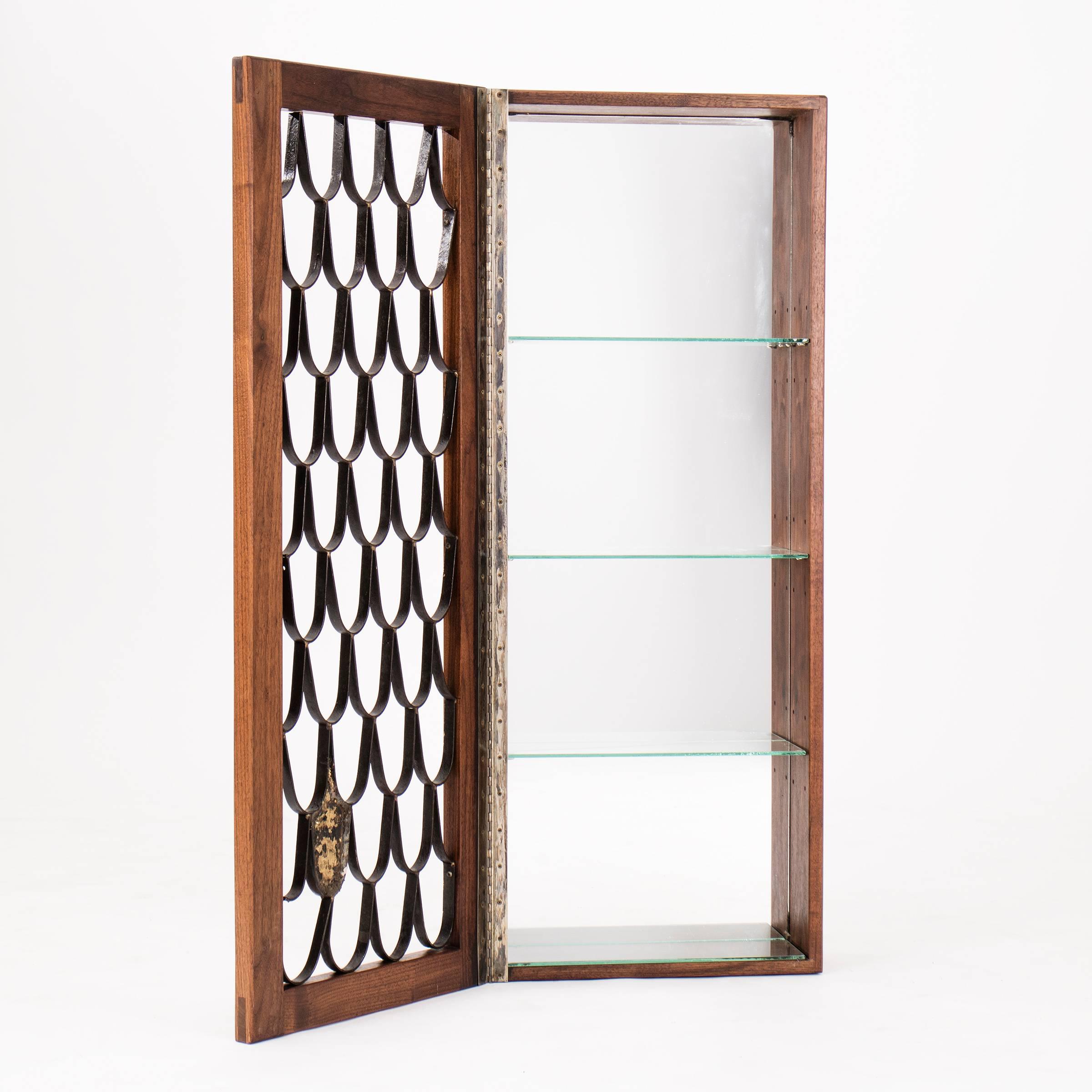Early collaboration from Paul Evans Studio and Phillip Lloyd Powell. Piano hinged door with fish scale screen, adjustable glass shelves and mirrored back panel. Wall-mounted by French cleat.