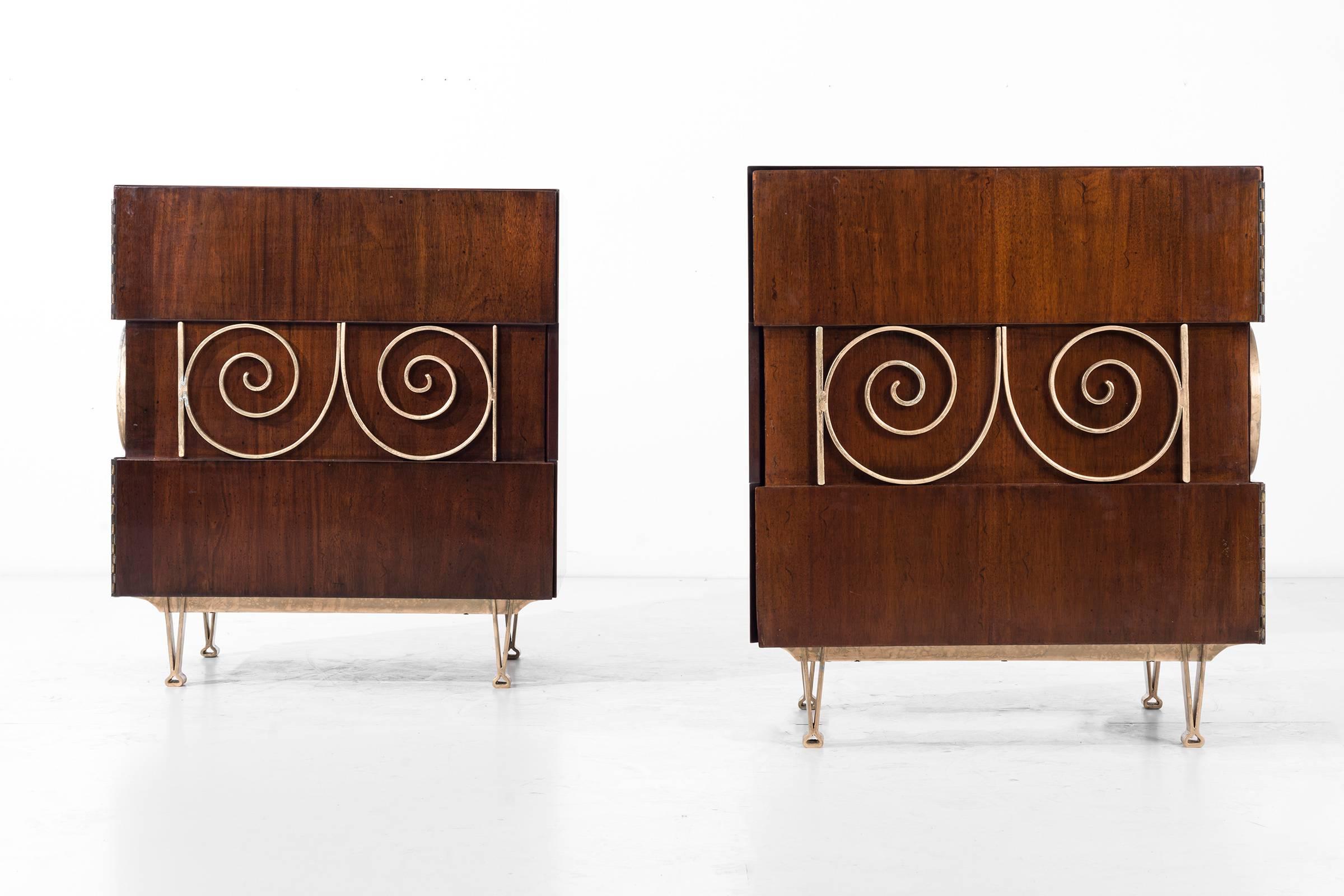 These end tables are covered in brass plated ornamentation, supported by brass V-shaped legs; the wood is mahogany and walnut fused together.