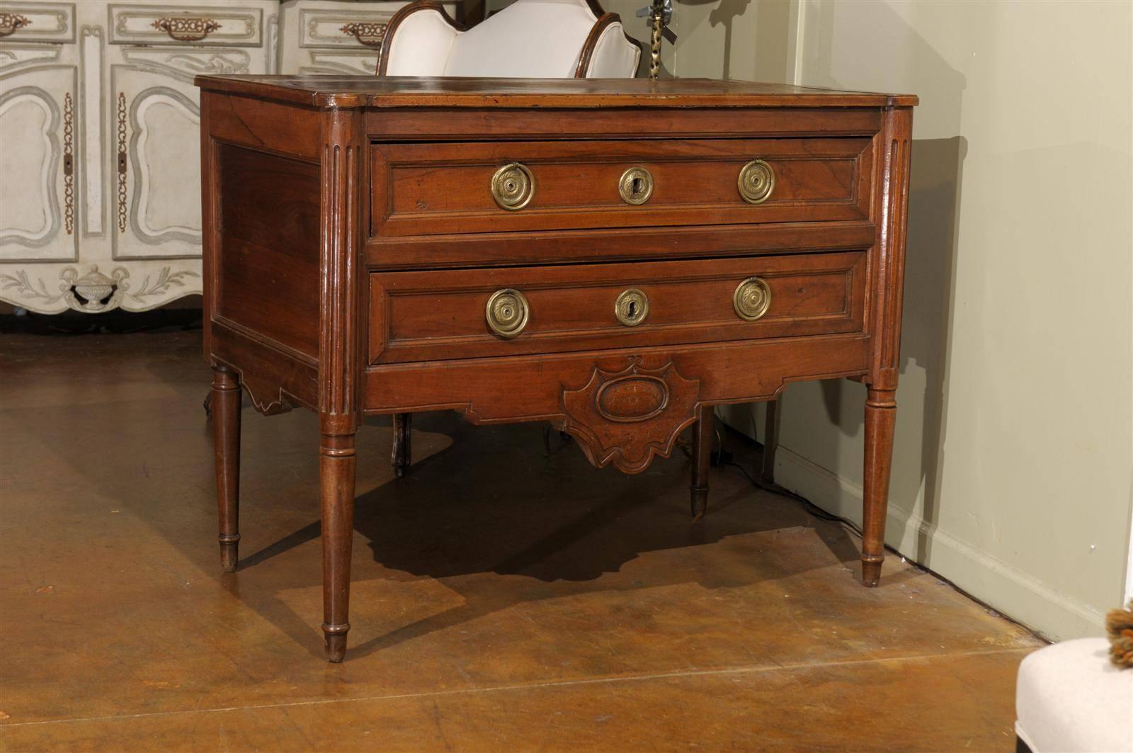 A French walnut Louis XVI style two-drawer commode from the 19th century. This French Louis XVI style walnut commode features a rectangular top with rounded corners in the front over two long dovetailed drawers with recessed panels. Each drawer is