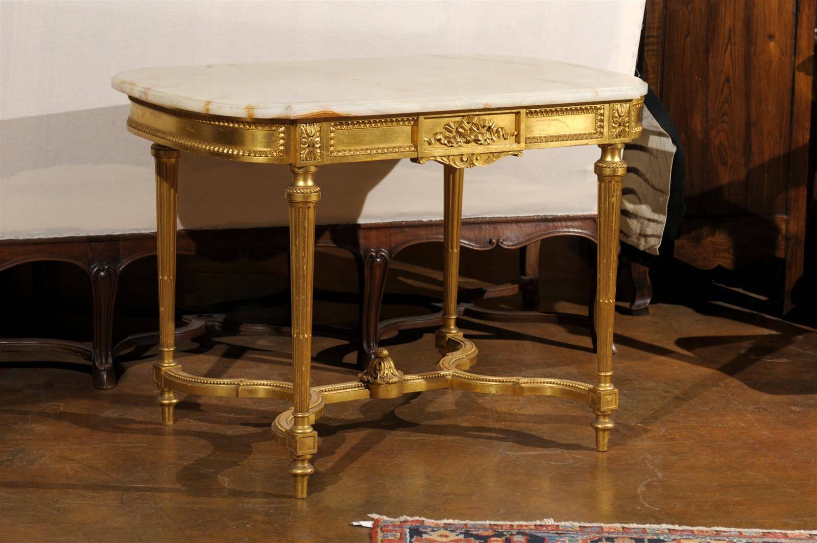 A French Louis XVI style center table with giltwood structure and onyx top from the 19th century. This exquisite French Louis XVI century center table features a shaped onyx top supported by a giltwood base. The carved apron is delicately adorned
