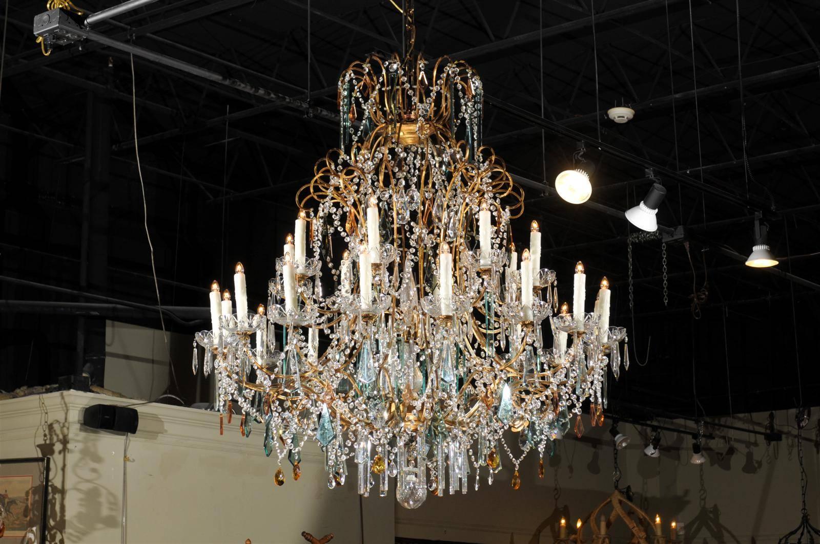 Continental Italian twenty-four light gilt, crystal and colored crystal chandelier, with two rows of gilt scrolling arms, surmounting two rows of scrolling arms ending in bell-form bobeches, the first having eight lights, the second having sixteen,