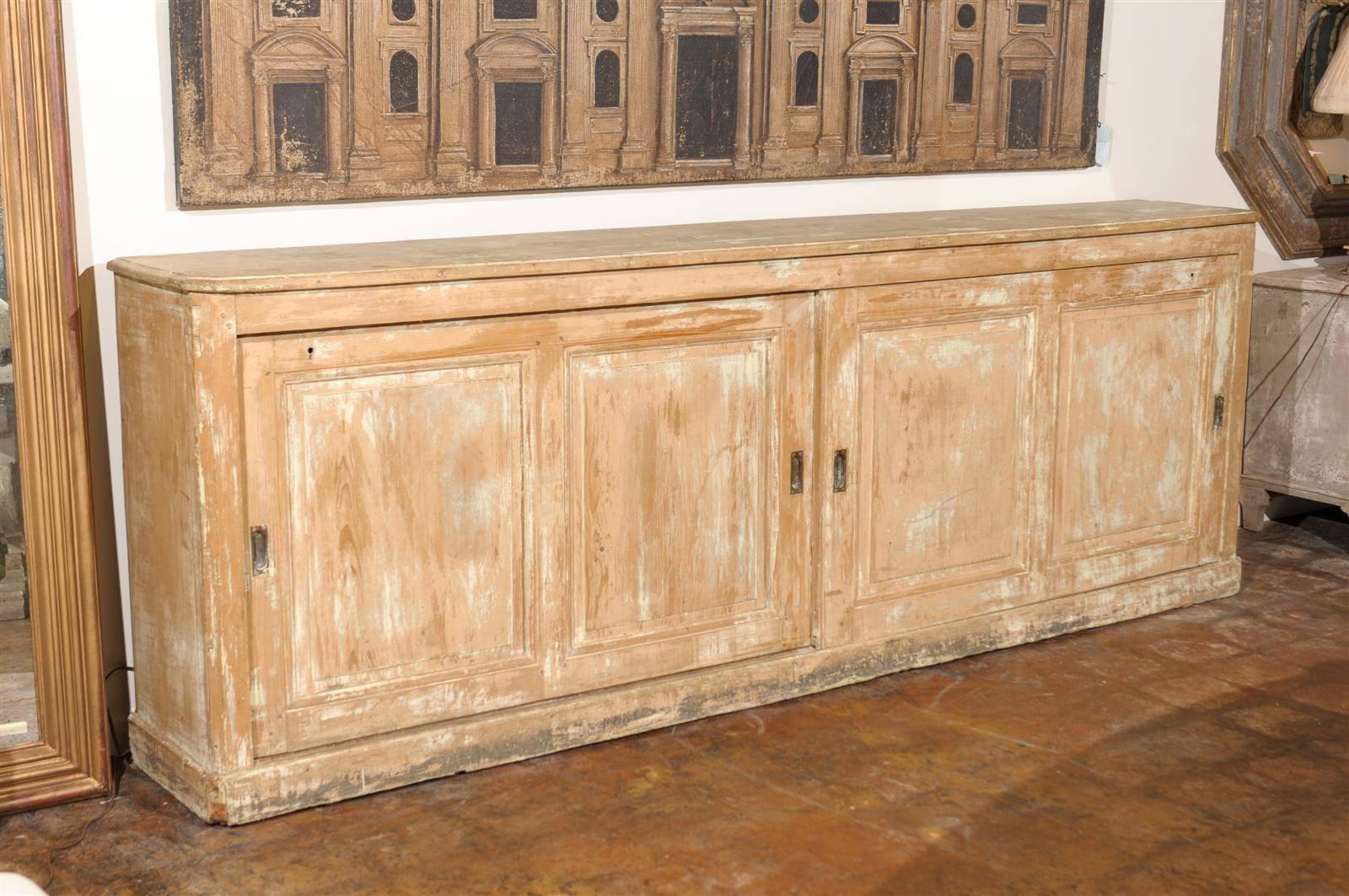 This Italian extra long wooden shop counter from Tuscany was born in the 19th century. It features a long and narrow rectangular top with rounded edges and canted corners as well as side posts. Sitting below are two sliding doors divided with two