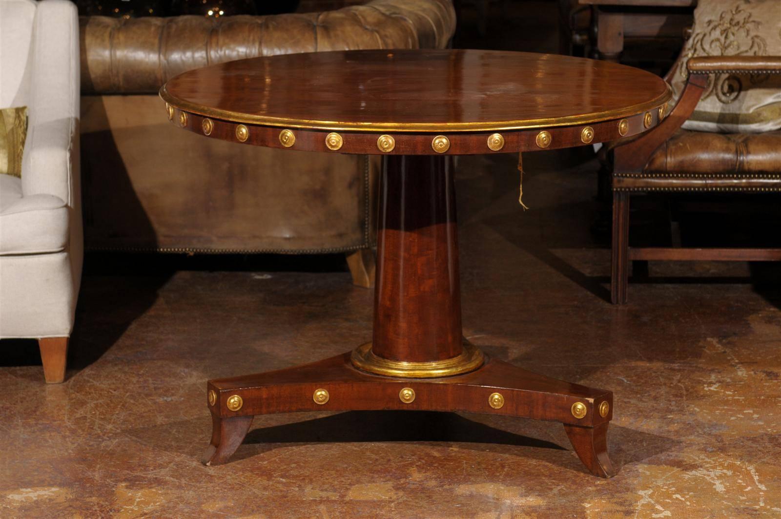 Early 19th century mahogany Empire period tilt-top pedestal center table, the circular top raised on a singular pedestal and ending in a triple base and splayed feet, with gilt accents throughout.
