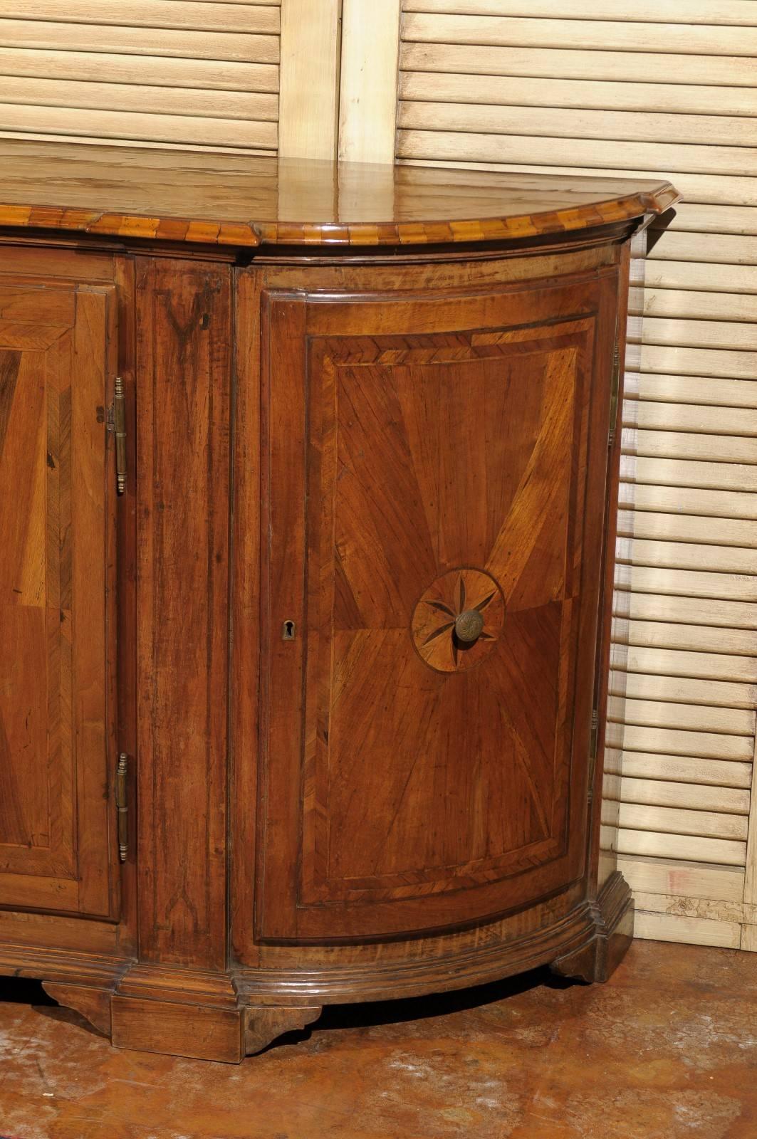 This exquisite Italian credenza from the mid 19th century features a beautiful walnut, satinwood and ebony inlaid body. The serpentine top is quarter-veneered with a delicate flower marquetry motif in its center and thin banding on the surround, and