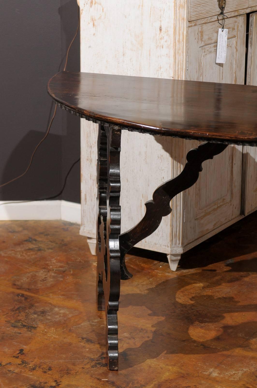 A pair of Tuscan Baroque style demi-lune console tables with lyre shaped legs from the mid 18th century. This pair of Italian carved walnut demi-lune tables features semi-circular tops over exquisitely carved lyre-shaped angled legs, reminiscent of