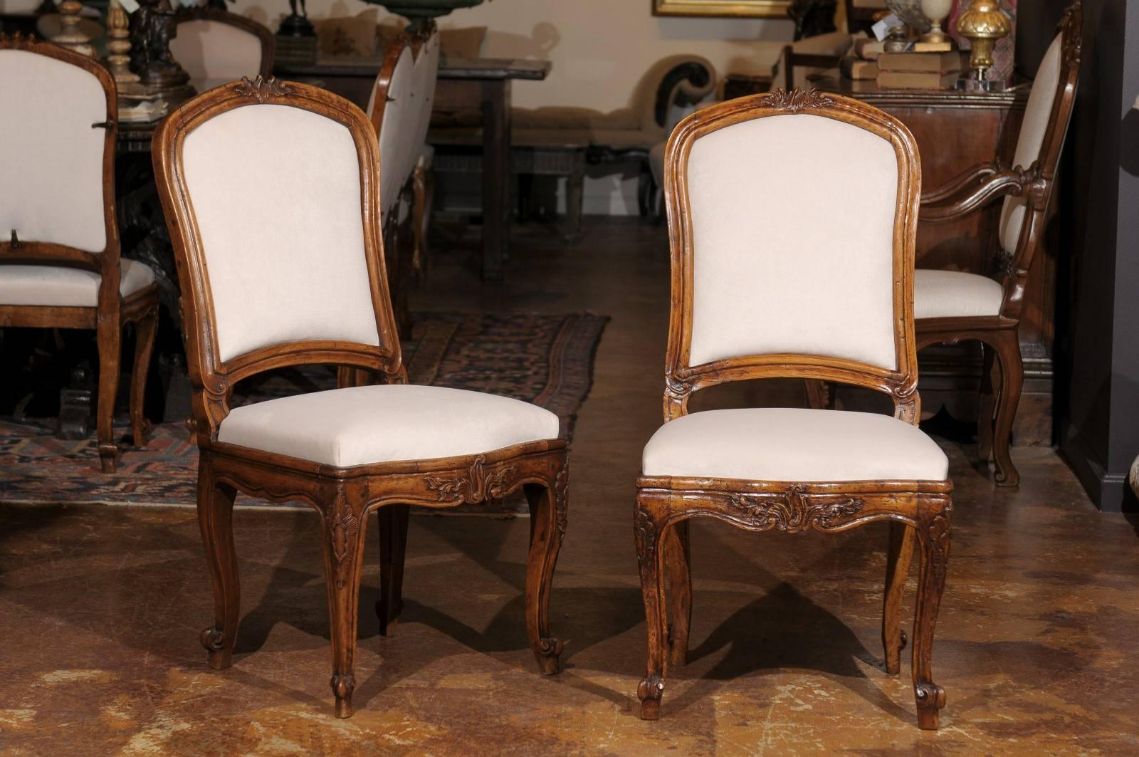A set of 12 Italian Louis XV style wooden carved dining chairs with upholstered backs and seats, from the late 19th century. This set of Italian dining chairs features slightly slanted and carved backs with Rocaille motifs at the crest. The lower