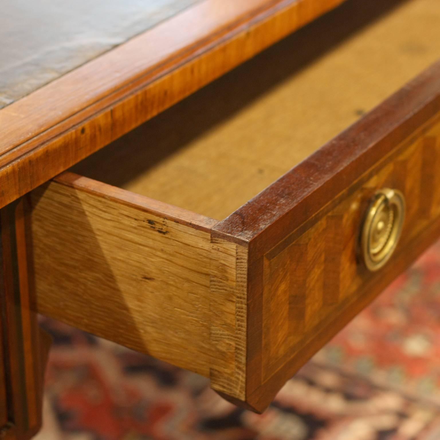 This French grand scale Louis XVI style kingwood and tulip inlaid bureau plat from the turn of the century (19th to 20th) features a dark leather lined writing desk above three dovetailed drawers with ring pulls over circular beaded back plates. The