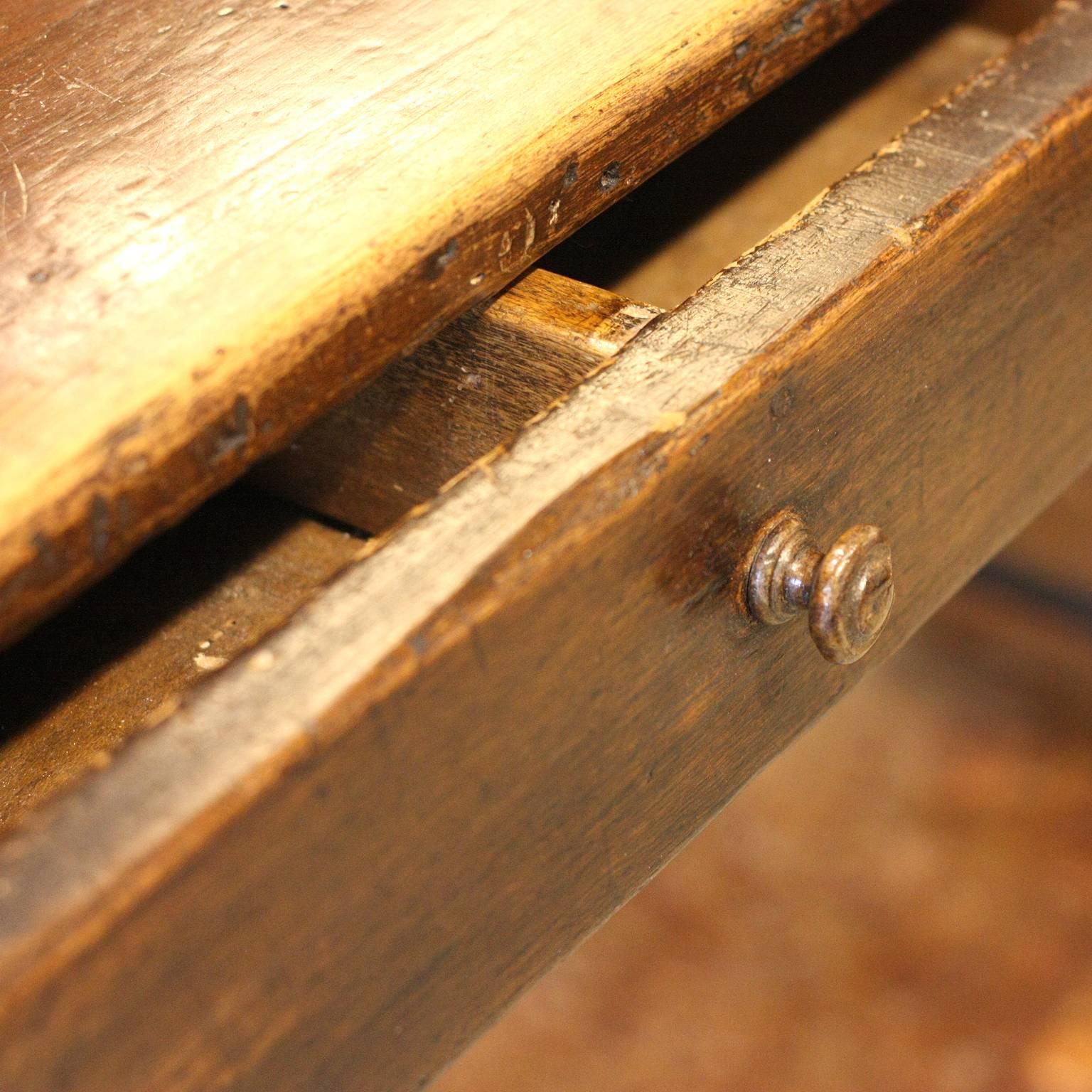 A French 18th century wooden farmhouse table with single drawer, straight legs and cross stretcher. This French farm table features a rectangular top overhanging a simple apron with small single drawer and inner divider. The table is raised on four