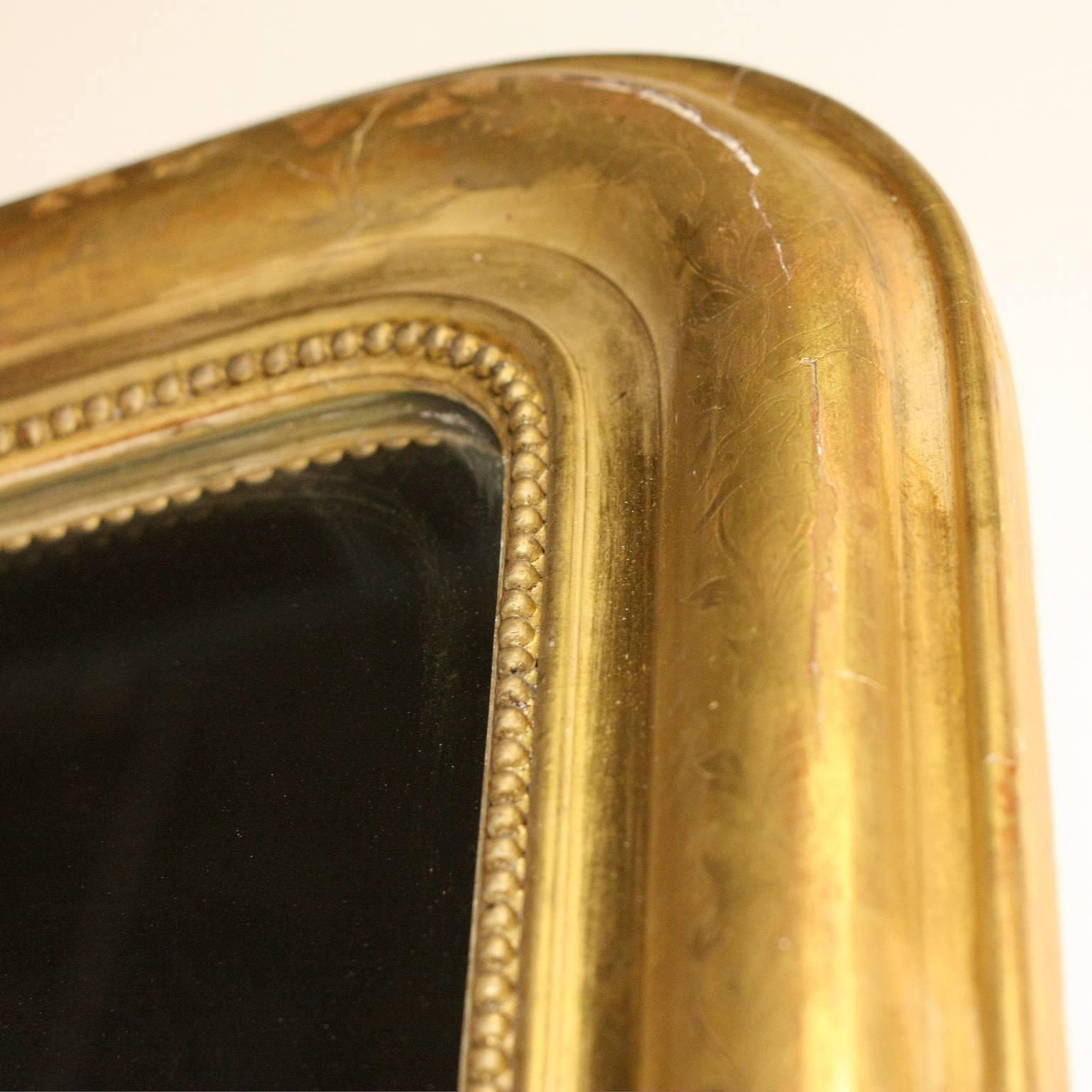 This large size French Louis-Philippe gilded mirror from the early 20th century features the typical rectangular Silhouette with rounded corners in the upper section. The outer part of the frame is etched with delicate vine motifs while the inner